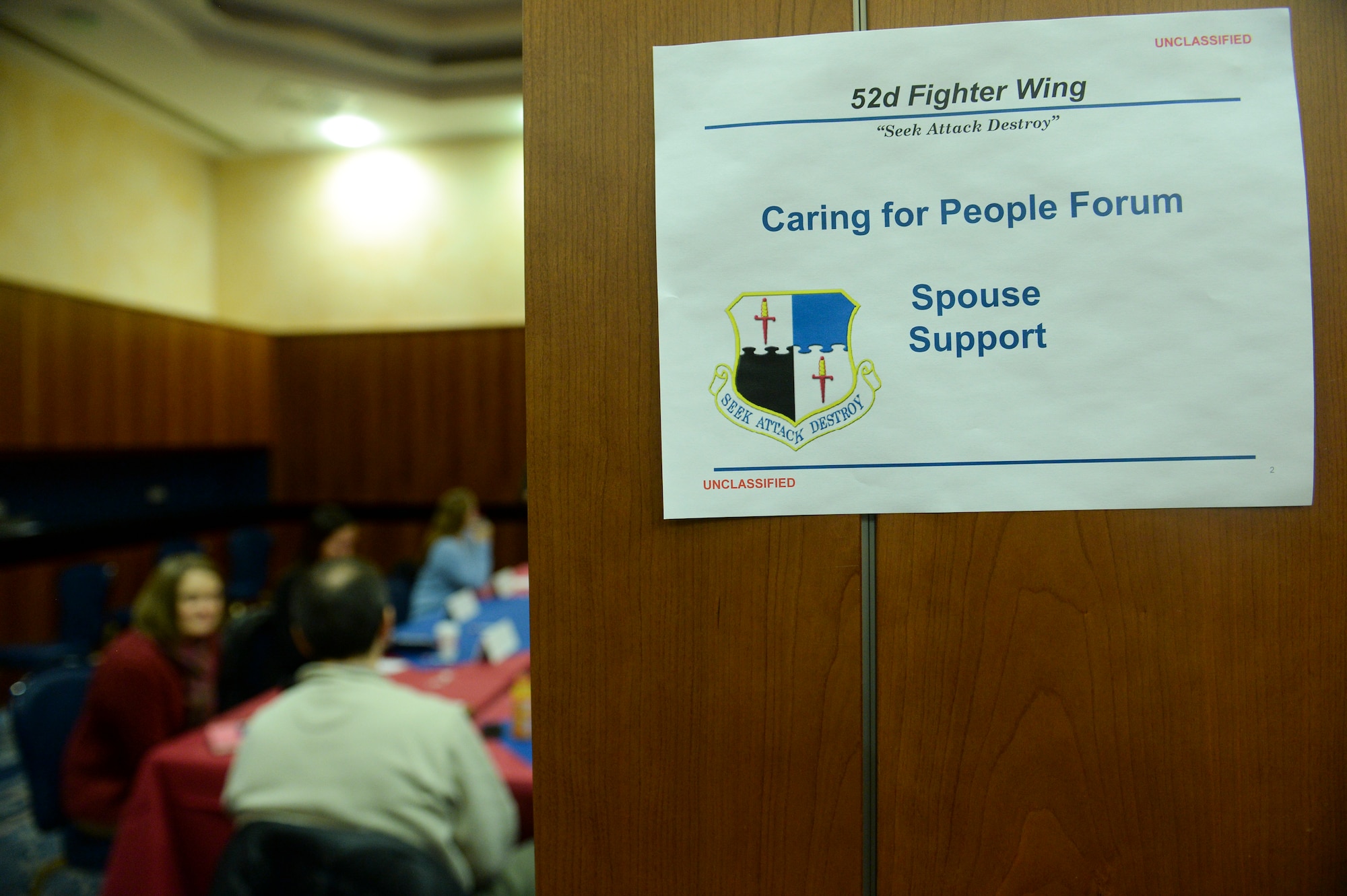 A Caring for People Forum sign hangs on a wall as members of Saber Nation talk during the Caring for People Forum Jan. 29, 2014, at Spangdahlem Air Base, Germany. The forum split the participants into six different groups, which included spouse support, single airmen support, health and fitness, child and youth activities, housing and school support. (U.S. Air Force photo by Senior Airman Rusty Frank/Released)