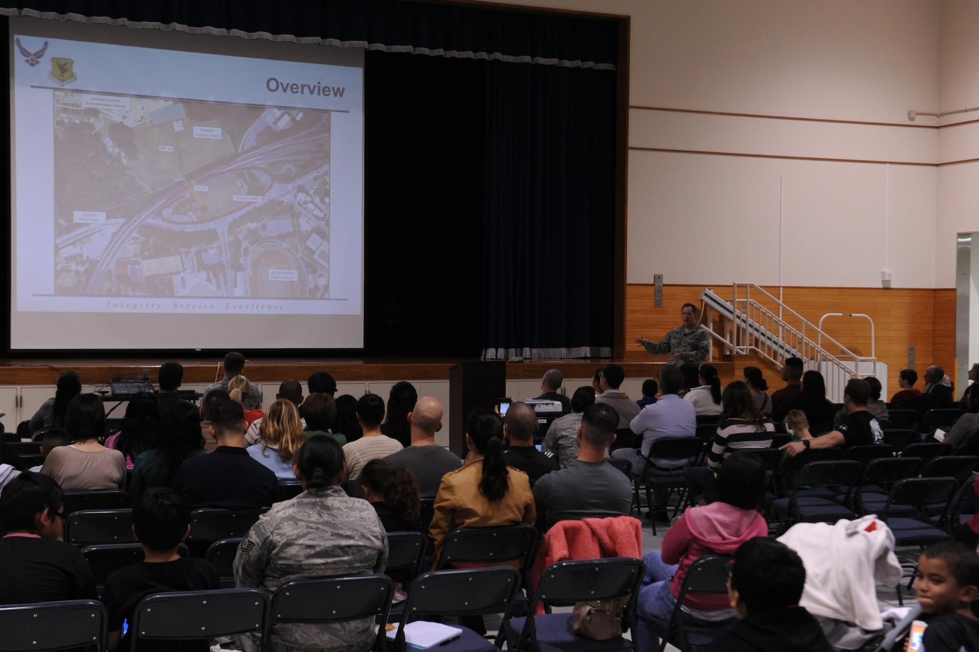U.S. service members and community members receive a brief on the discovery and excavation of 30-gallon barrels from the Okinawa City soccer field at a town hall meeting on Kadena Air Base, Japan, Jan. 28, 2014. The meeting was held to address concerns of local community members and discuss the area's safety, tests conducted on samples of soil, air and water, the history of the location, and future actions. (U.S. Air Force photo by Senior Airman Malia Jenkins) 