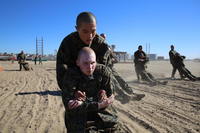 Recruit Minki Lee, Platoon 1069, Company D, 1st Recruit Training Battalion, buddy drags a fellow recruit after the obstacle course aboard the depot Jan. 17. Each time the recruits run through the course, they wear extra gear to simulate a combat situation.