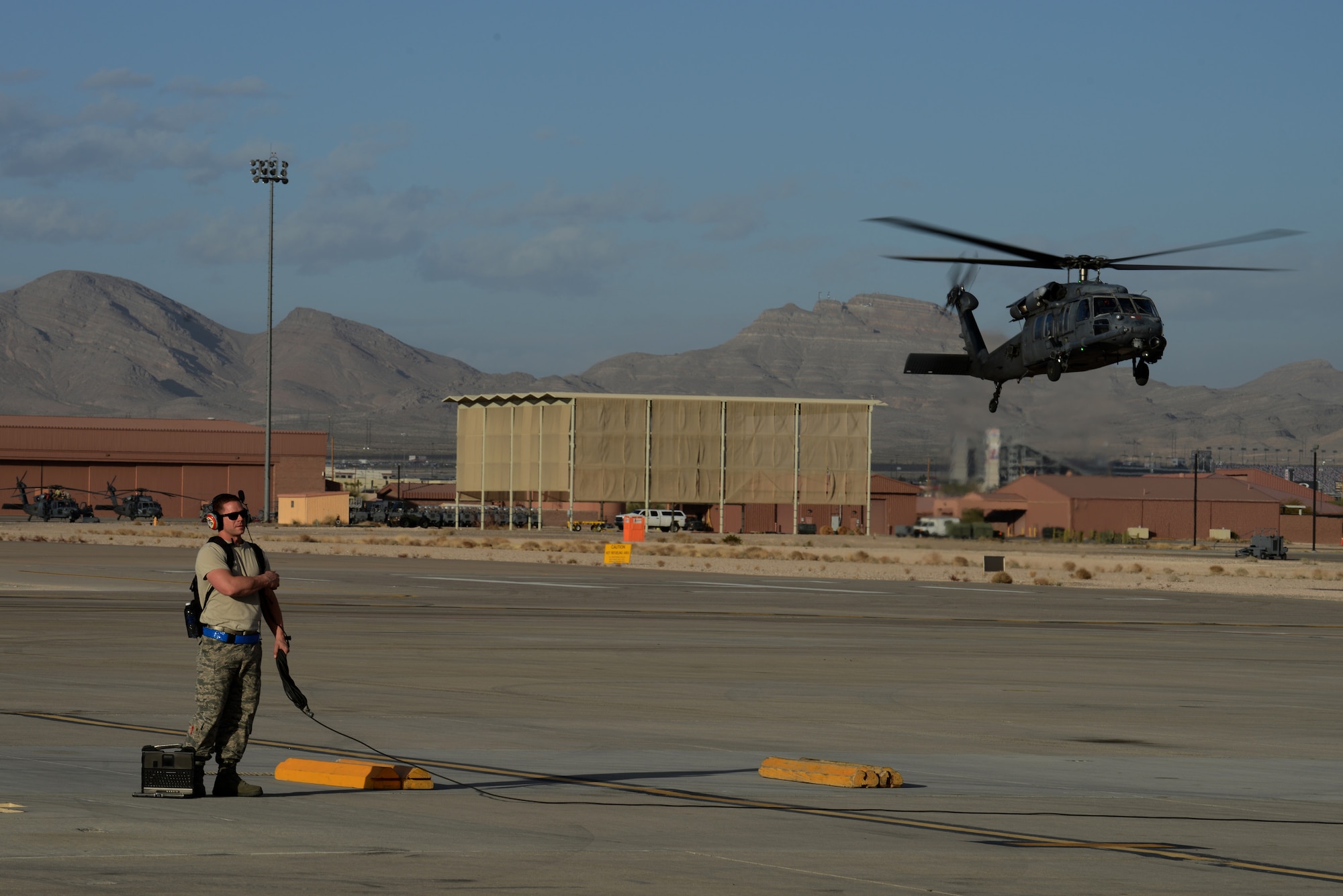 Tech. Sgt. Mike Friend, 22nd Aircraft Maintenance Squadron flying crew chief from McConnell Air Force Base, Kan., prepares the parking area for an incoming KC-135 Stratotanker while an HH-60 Pave Hawk from the 66th Rescue Squadron, Nellis AFB, Nev., hovers in the background here Jan 30, 2014. Friend is one of more than 3,200 military members currently participating in the combat exercise Red Flag 14-1. By providing realistic combat training in a contested, degraded and operationally limited environment, Red Flag 14-1 provides pilots with real-time combat scenarios and helps ground crews test their readiness capabilities. (U.S. Air Force photo by Senior Airman Benjamin Sutton/Released)