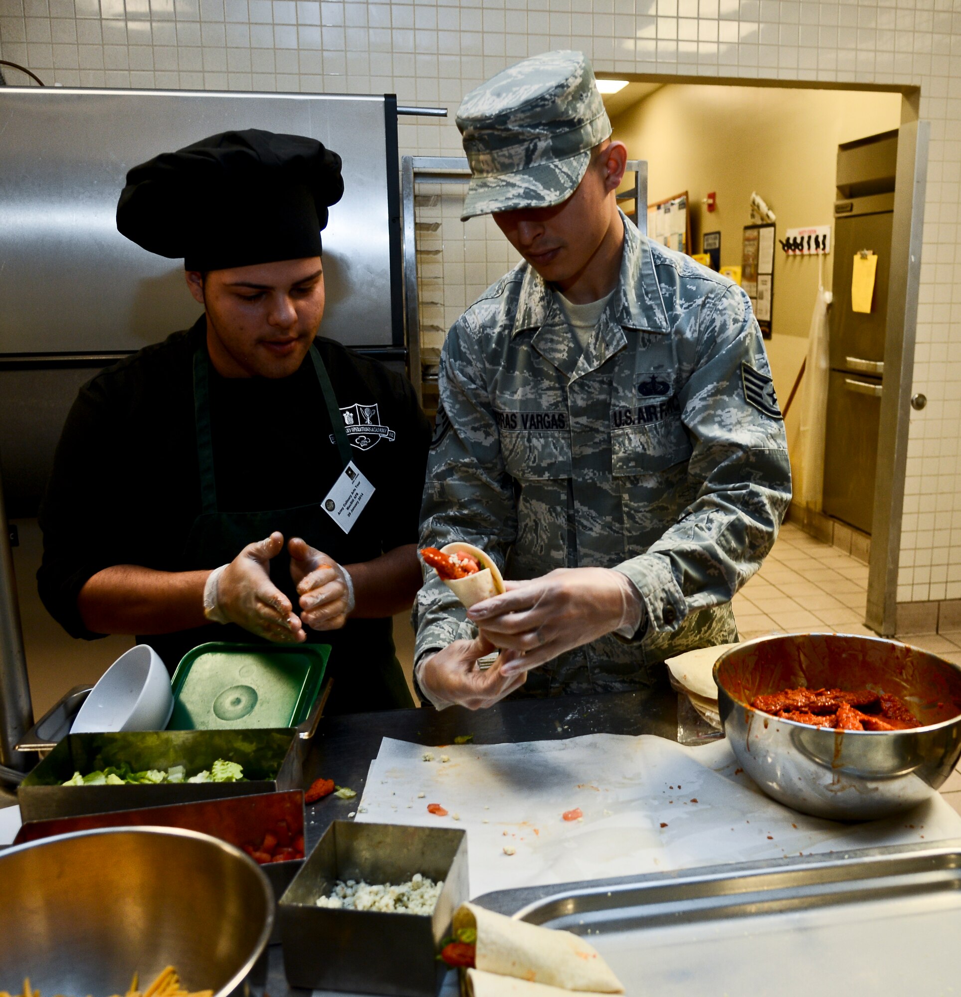Staff Sgt. Luis Porras-Vargas shows Fernando Gomez, Chamberlain High School student,  how to properly wrap a tortilla for a buffalo chicken wrap at the Diners Reef on MacDill Air Base, Fla. The students learned industry standard recipes, next day menu preparation, and culinary arts skills. (U.S. Air Force photo by Senior Airman Melanie Bulow-Gonterman/Released)  