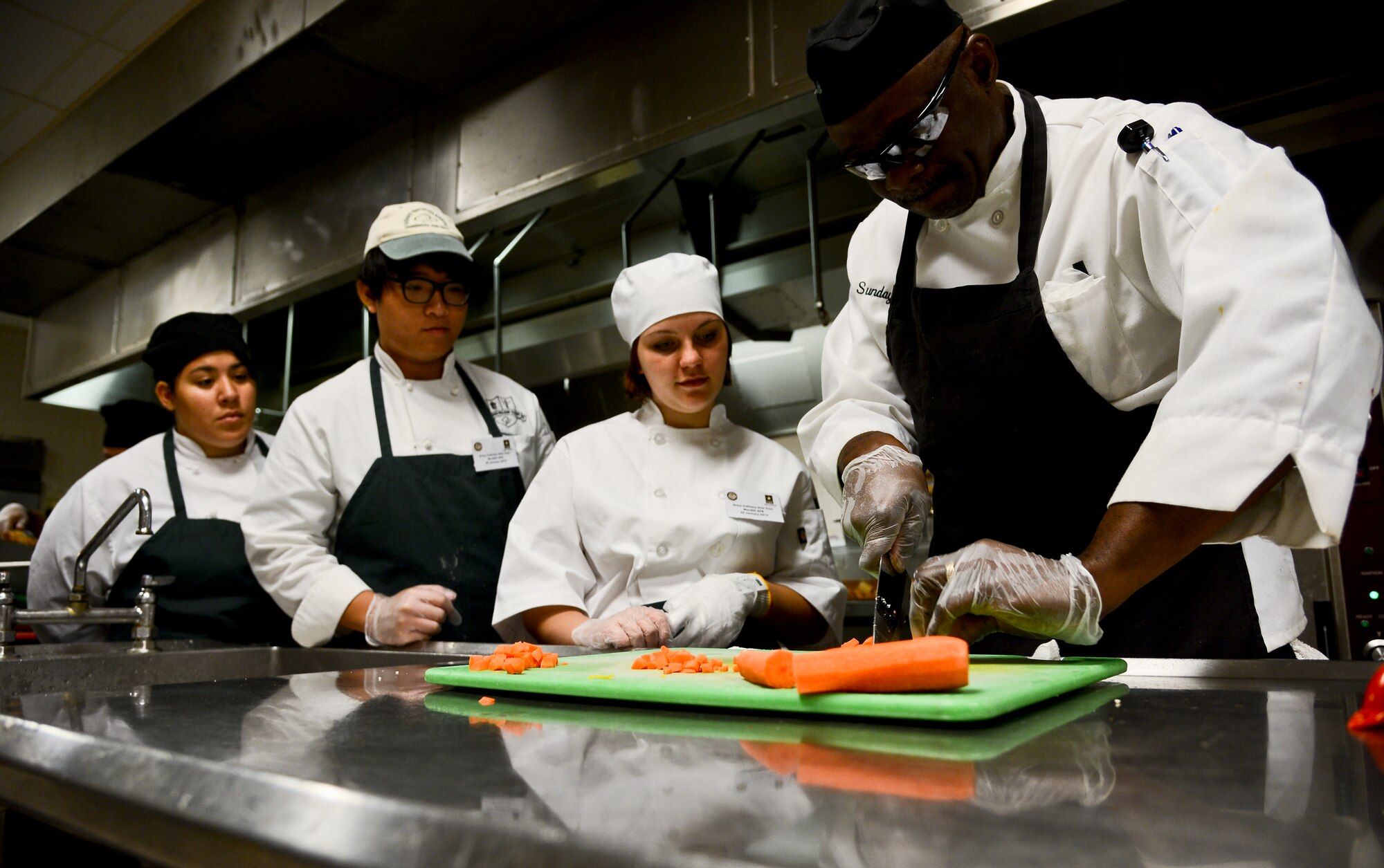 Sunday Padonu, 6th Force Support Squadron assitant excecutive chef, teaches students from Chamberlain High School how to effectively cut vegtables at the Diner’s Reef on MacDill Air Base, Fla. The students learned industry standard recipes, next day menu preparation, and culinary art skills such as different types of cutting, slicing, dicing and serving techniques. (U.S. Air Force photo by Senior Airman Melanie Bulow-Gonterman/Released)  