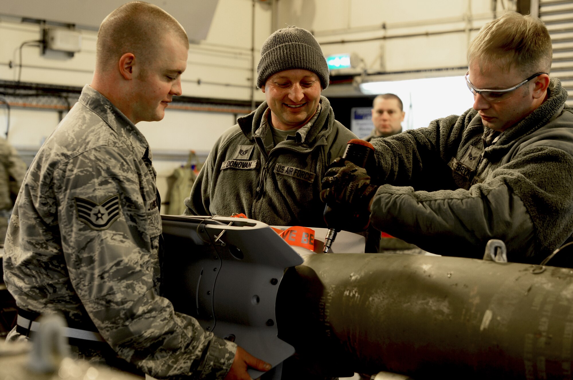 Staff Sgts. Seth Johnston and James Donovan, 48th Munitions Squadron dedicated crew chiefs, and Senior Airman Timothy Bryk, 48th MUNS crew member, mount a fin to a GBU-12 laser-guided bomb, Jan. 29, 2014, on Royal Air Force Lakenheath, England. The 48th MUNS Airmen are building the 500-pound bombs in preparation for an upcoming exercise. (U.S. Air Force photo by Airman 1st Class Dawn M. Weber/Released)