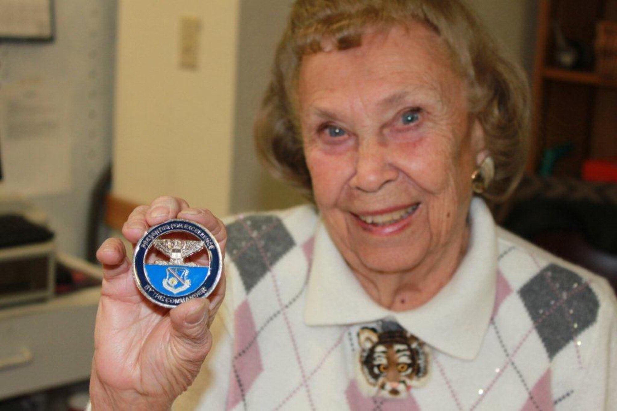 Delores Dicker, a volunteer at the Kirtland Spouses’ Club Thrift Shop, displays a coin, given to her by Col. Tom Miller, 377th Air Base Wing commander during a surprise 90th birthday celebration. Dicker has been volunteering at the thrift shop for 28 years. (Photo by Meredith Mingledorff)