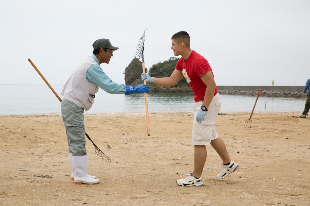 Cpl. Ricardo Gonzalez, right, is handed a rake from Yoshihisa Asahi during a beach cleanup May 20, 2014, at Matsuda-no-Hama Beach. Gonzalez has been chosen by the American Legion to receive the Spirit of Service Award at a national convention Aug. 26, 2014, in Charlotte, North Carolina. Gonzalez is a San Jose, California, native and Marine Air-Ground Task Force planning specialist with Headquarters Company, 4th Marine Regiment, 3rd Marine Division, III Marine Expeditionary Force. 
