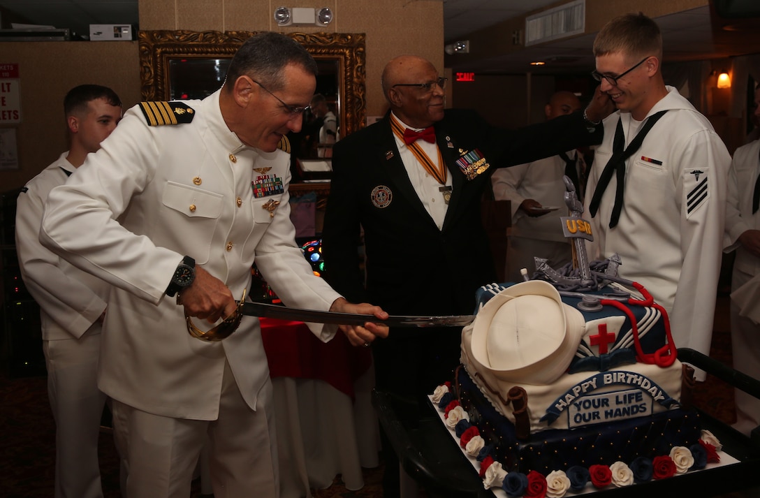 Navy Capt. David A. Lane, Naval Hospital Camp Lejeune commanding officer, retired Maj. James Capers, guest of honor, and the youngest corpsman cut a cake celebrating the 116th birthday of the U.S. Naval Hospital Corps aboard the Henrietta III river boat in Wilmington, N.C., June 14.