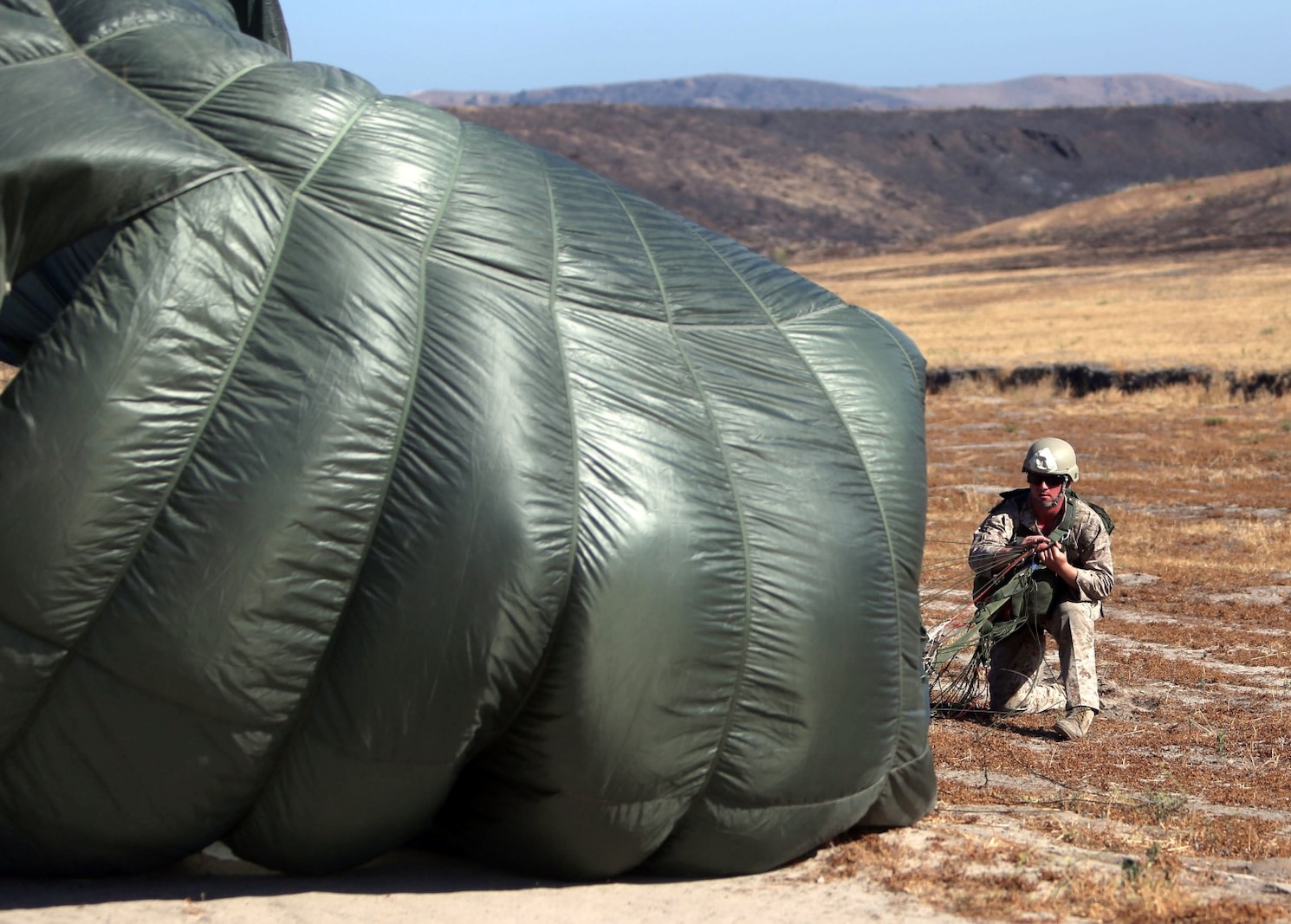 A Marine with Company C, 1st Reconnaissance Battalion, wrestles his parachute to the ground after landing from a static line jump aboard Marine Corps Base Camp Pendleton, Calif., June 25, 2014. The company practiced both freefall and static line jumps from a CH-43E helicopter to better prepare for potential combat operations anywhere they are needed worldwide.