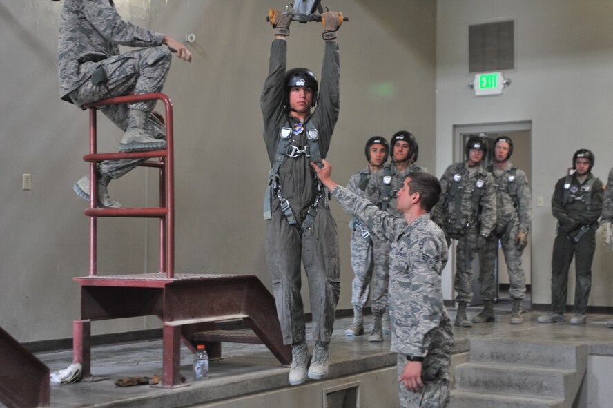 Airman 1st Class Zachary Rumke and A1C Lake Thompson, 22nd Training Squadron Survival, Evasion, Resistance and Escape specialist, demonstrate how to properly hold onto a zip line that will help the students simulate landing safely during parachute training at Fairchild Air Force Base, Washington, June 27, 2014.  The 22nd TRS parachute training tests, evaluates, demonstrates and instructs emergency egress parachute systems for Air Force aircrew career fields. (U.S. Air Force photo by Staff Sgt. Alexandre Montes)