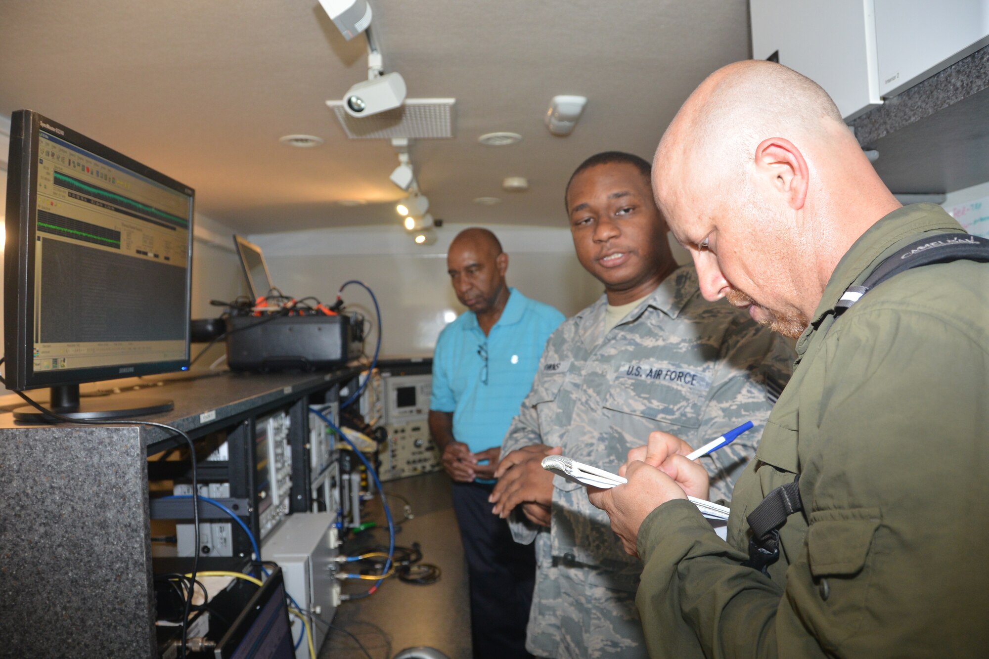 Staff Sgt. Michael Downs (forefront), emissions security technician and Wayne Jackson, emissions security lead, both from the 346th Test Squadron, Joint Base San Antonio-Lackland, Texas, talk with Daniel Terdiman, a CNET News senior writer, in a Mobile Assessment Vehicle. Downs explains how the team captures emanations with the use of their specialized equipment.  The test squadron used one of the 433rd Airlift Wing’s C-5A Galaxy aircraft July 26, 2014 as a test aircraft to assist technicians in demonstrating to how they provide that protection to military assets.  (U.S. Air Force photo/Minnie L. Jones)