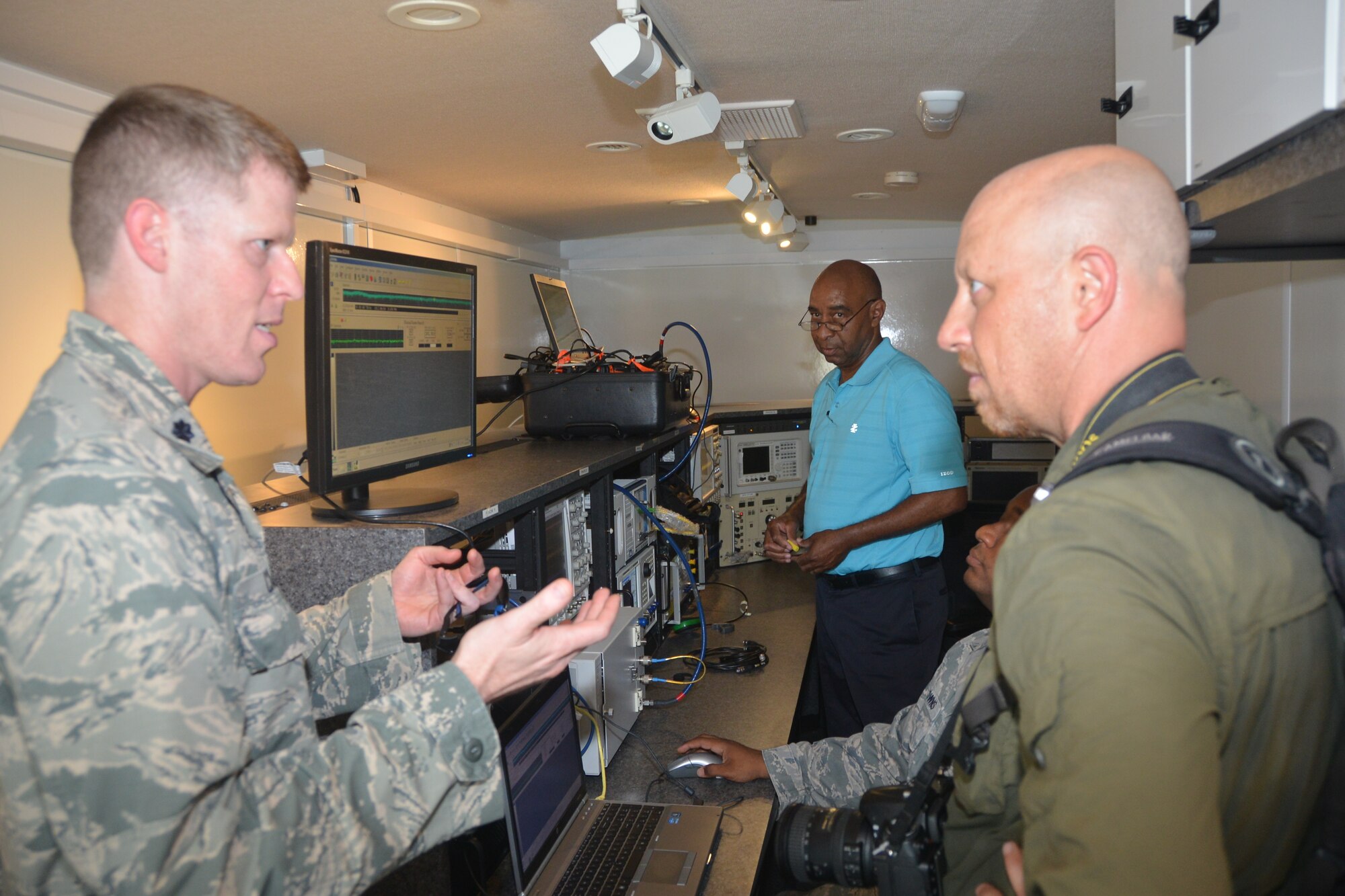 Lt. Col. Brendan Casey, commander 346th test squadron, Joint Base San Antonio-Lackland, Texas, talks with Daniel Terdiman senior writer from C-NET News.  In the background, Staff Sgt. Michael Downs, emissions security technician, Joint Base San Antonio-Lackland, Texas, scans the frequency range searching for any unintended emissions coming off of the target laptop while Wayne Jackson looks on providing technical assistance.  The 346th Test Squadron performs emissions security tests as part of the mission assurance assessment necessary for aircraft to return to the field after undergoing modifications.