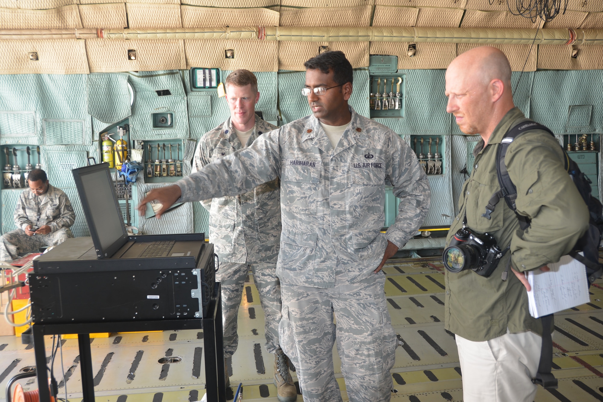 Maj. Anil Hariharan (forefront), 346thTest Squadron, Joint Base San Antonio-Lackland, Texas points to a screen on a laptop to Daniel Terdiman, senior writer from C-NET News, which has a sample output of random letters forming the outline of an "E."  The goal of the demo is to capture electromagnetic (EM) emanations from the equipment on the C-5A Galaxy aircraft. The test squadron used one of the 433rd Airlift Wing’s C-5A Galaxy aircraft at Joint Base San Antonio-Lackland, Texas July 26, 2014 as a backdrop and test aircraft to assist technicians in demonstrating to C-NET News how they provide that protection.  