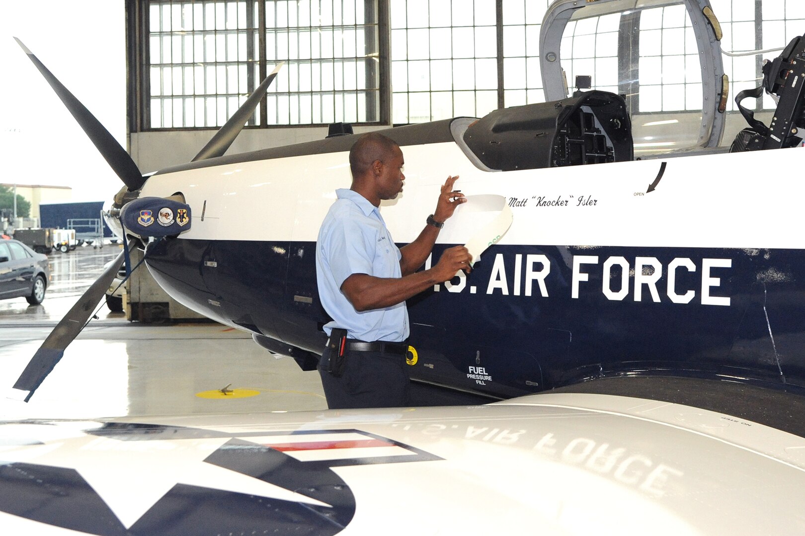 Mr. Louis Marcy, a member of the 12th Flying Training Wing Maintenance Directorate, unveils Col. Matthew C. Isler's name on a T-6 aircraft during the change of command ceremony here June 25. As part of an Air Force tradition, one of the aircraft is painted with the new commander's name.  (U.S. Air Force photo by Melissa Peterson)