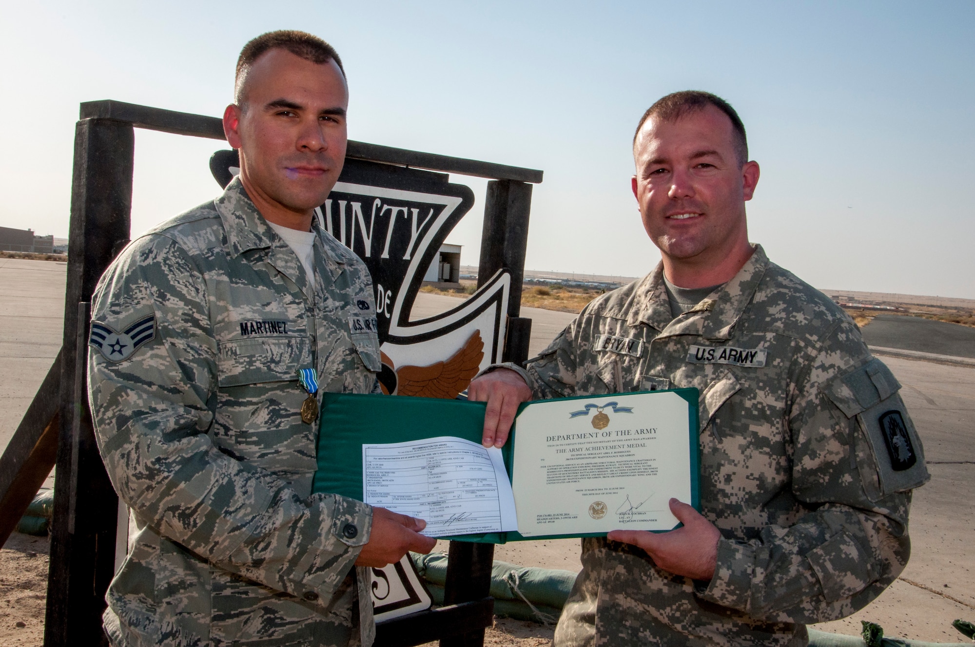 Air Force Senior Airman Loren Martinez, 386th Expeditionary Maintenance Squadron aircraft metals technician, received an Army Achievement Medal from Army Chief Warrant Officer 3 Shawn Bryan, Bravo Company 3-159th Attack Reconnaissance Battalion test pilot June 28, 2014 close to the fightline at The Rock in Southwest Asia. Martinez and two other maintainers were responsible for structural and composite repairs on a dozen AH-64Ds ensuring the aircraft were mission ready. Martinez, from Baldwin Park, California, deployed from the 146th Airlift Wing, Channel Islands Air National Guard Station, California, in support of Operation Enduring Freedom. (U.S. Air Force photo by Senior Master Sgt. Allison Day)