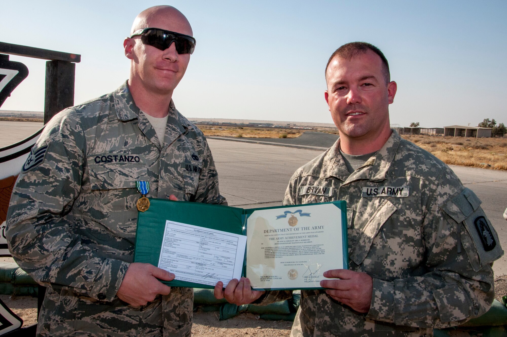 Air Force Staff Sgt. Justin Costanzo, 386th Expeditionary Maintenance Squadron aircraft metals technician, received an Army Achievement Medal from Army Chief Warrant Officer 3 Shawn Bryan, Bravo Company 3-159th Attack Reconnaissance Battalion test pilot June 28, 2014 close to the fightline at The Rock in Southwest Asia. Costanzo and two other maintainers were responsible for structural and composite repairs on a dozen AH-64Ds ensuring the aircraft were mission ready. Costanzo deployed from the 146th Airlift Wing, Channel Islands Air National Guard Station, California, in support of Operation Enduring Freedom and is a native of Washingtonville, New York. (U.S. Air Force photo by Senior Master Sgt. Allison Day)