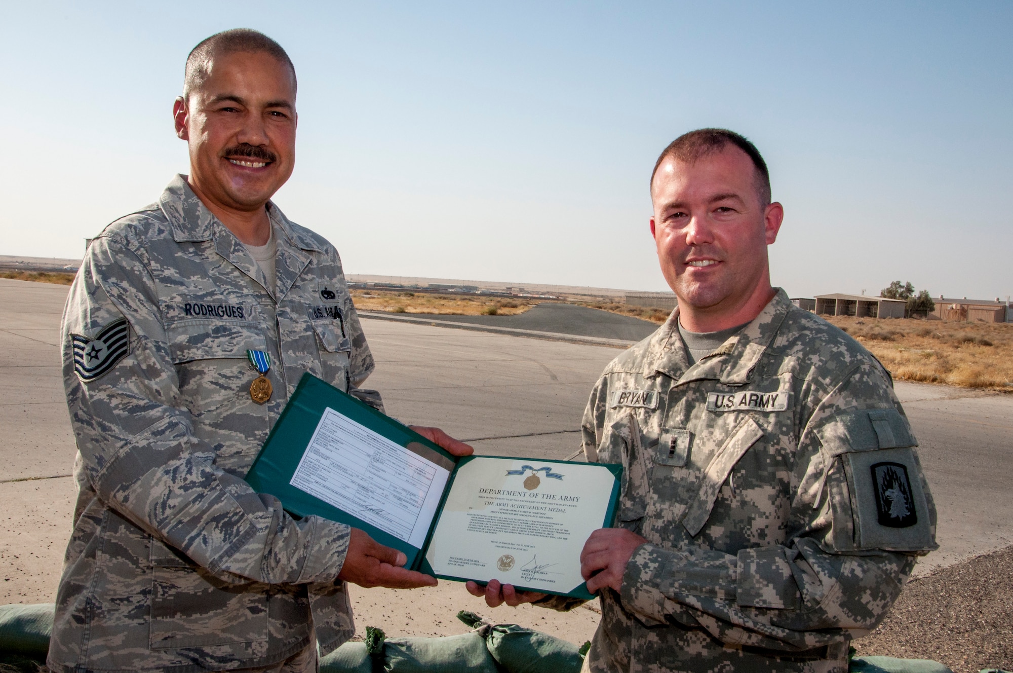 Air Force Tech. Sgt. Abel Rodrigues, 386th Expeditionary Maintenance Squadron aircraft structures technician, received an Army Achievement Medal from Army Chief Warrant Officer 3 Shawn Bryan, Bravo Company 3-159th Attack Reconnaissance Battalion test pilot June 28, 2014 close to the fight line at The Rock in Southwest Asia. Rodrigues and two other maintainers were responsible for structural and composite repairs on a dozen AH-64Ds ensuring the aircraft were mission ready. He deployed from the 146th Airlift Wing, Channel Islands Air National Guard Station, California, in support of Operation Enduring Freedom a and is a native of La Palma, California (U.S. Air Force photo by Senior Master Sgt. Allison Day)