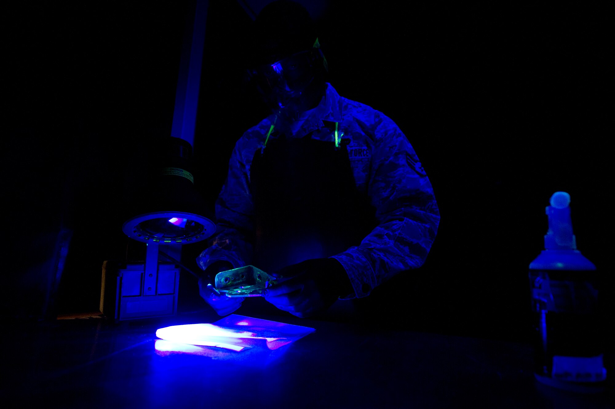 Senior Airman Roderick Johnson, 49th Maintenance Squadron non-destructive inspection technician, inspects a metal bracket coated with fluorescent penetrant at Holloman Air Force Base, N.M., June 30. The item is dipped in a very low viscosity penetrant which fills any voids left by cracks or damage and indicates a need for repair. After the penetrant is applied, it is placed on a surface for a specific period of time to allow the penetrant to create a visible indication of damage under a black light. NDI technicians are able to assist aircraft maintainers by identifying damage to aircraft parts in a non-destructive manner, allowing them to ensure military aviation equipment safety. (U.S. Air Force photo by Airman 1st Class Aaron Montoya / Released)