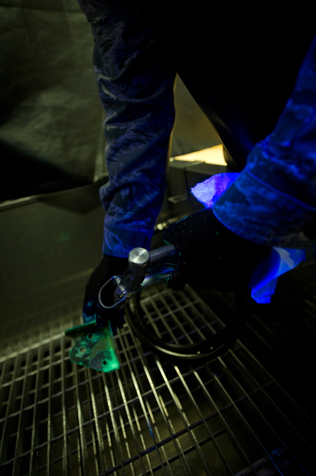 Senior Airman Roderick Johnson, 49th Maintenance Squadron non-destructive inspection technician, prepares a metal bracket for a closer inspection under fluorescent lighting at Holloman Air Force Base, N.M., June 30. The item is dipped in a very low viscosity penetrant which fills any voids left by cracks or damage and indicates a need for repair. After the penetrant is applied, it is placed on a surface for a specific period of time to allow the penetrant to create a visible indication of damage, afterward the part is carefully cleaned. NDI technicians are able to assist aircraft maintainers by identifying damage to aircraft parts in a non-destructive manner, allowing them to ensure military aviation equipment safety. (U.S. Air Force photo by Airman 1st Class Aaron Montoya / Released)