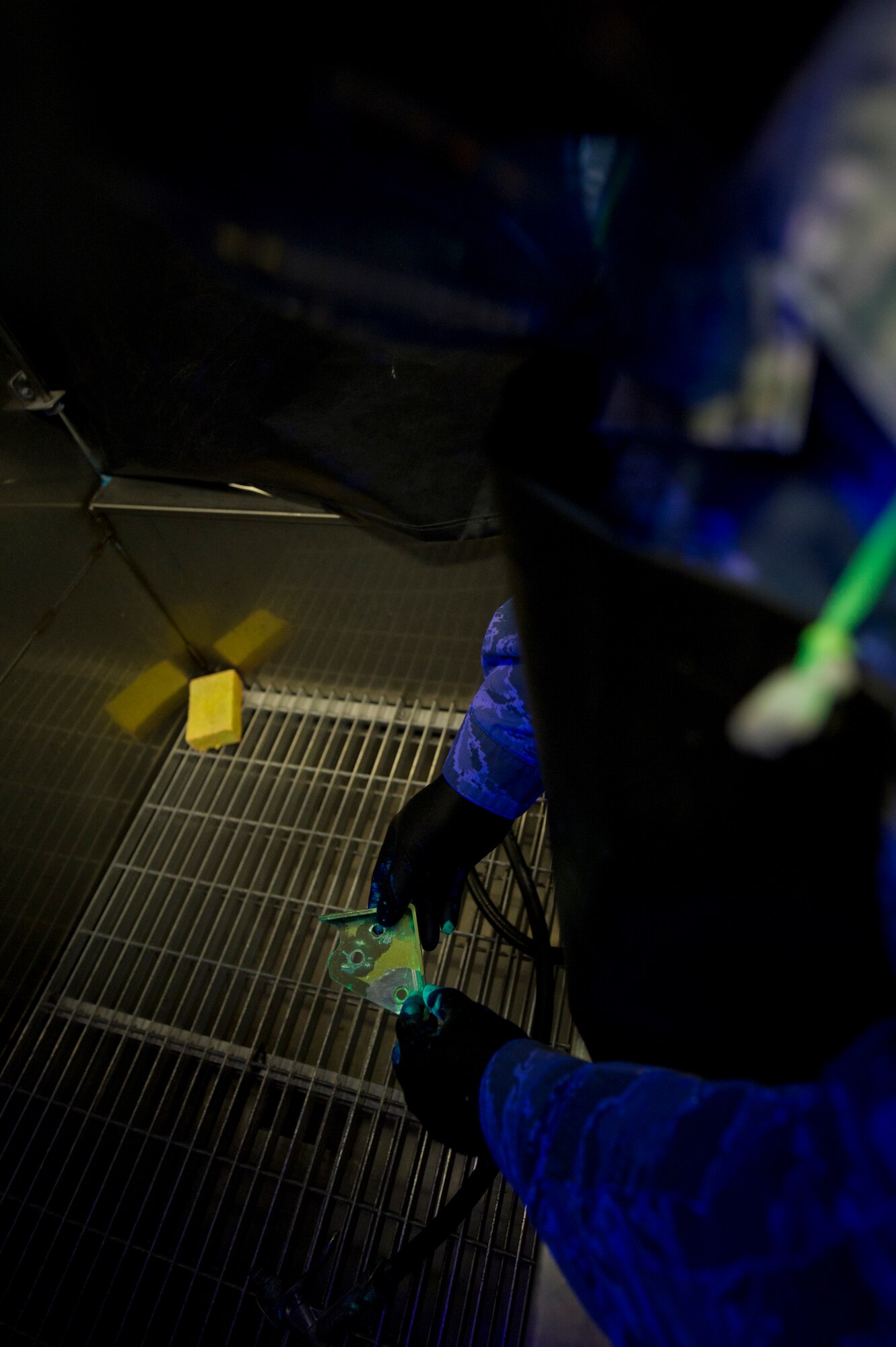 Senior Airman Roderick Johnson, 49th Maintenance Squadron non-destructive inspection technician, prepares a metal bracket for a closer inspection under fluorescent lighting at Holloman Air Force Base, N.M., June 30. The item is dipped in a very low viscosity penetrant which fills any voids left by cracks or damage and indicates a need for repair. After the penetrant is applied, it is placed on a surface for a specific period of time to allow the penetrant to create a visible indication of damage. NDI technicians are able to assist aircraft maintainers by identifying damage to aircraft parts in a non-destructive manner, allowing them to ensure military aviation equipment safety. (U.S. Air Force photo by Airman 1st Class Aaron Montoya / Released)