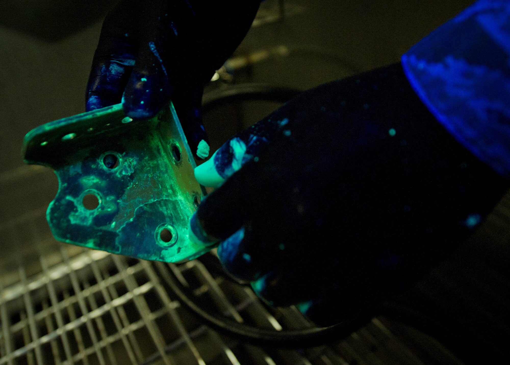 Senior Airman Roderick Johnson, 49th Maintenance Squadron non-destructive inspection technician, prepares a metal bracket for a closer inspection under fluorescent lighting at Holloman Air Force Base, N.M., June 30. The item is dipped in a very low viscosity penetrant which fills any voids left by cracks or damage and indicates a need for repair. After the penetrant is applied, it is placed on a surface for a specific period of time to allow the penetrant to create a visible indication of damage. NDI technicians are able to assist aircraft maintainers by identifying damage to aircraft parts in a non-destructive manner, allowing them to ensure military aviation equipment safety. (U.S. Air Force photo by Airman 1st Class Aaron Montoya / Released)
