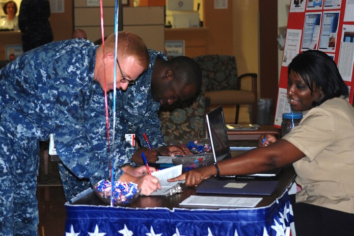 Petty Officer 1st Class Dale Oliver, Naval Health Clinic Charleston pharmacy technician and assistant voting officer (right), explains the write-in ballot option to Petty Officer 1st class John Furr (left), as Petty Officer 2nd Class Gregory Bethel fills out a voter registration form. NHCC’s voting assistance officers set up the voter registration table in the NHCC atrium during Armed Forces Voters Week which began June 30 and runs through  July 7, to assist service members in registering to vote or to request an absentee ballot for this year’s elections. Military voters still have the option to send in a write-in ballot even if they haven't registered to vote. (U.S. Navy photo/by Kris Patterson)