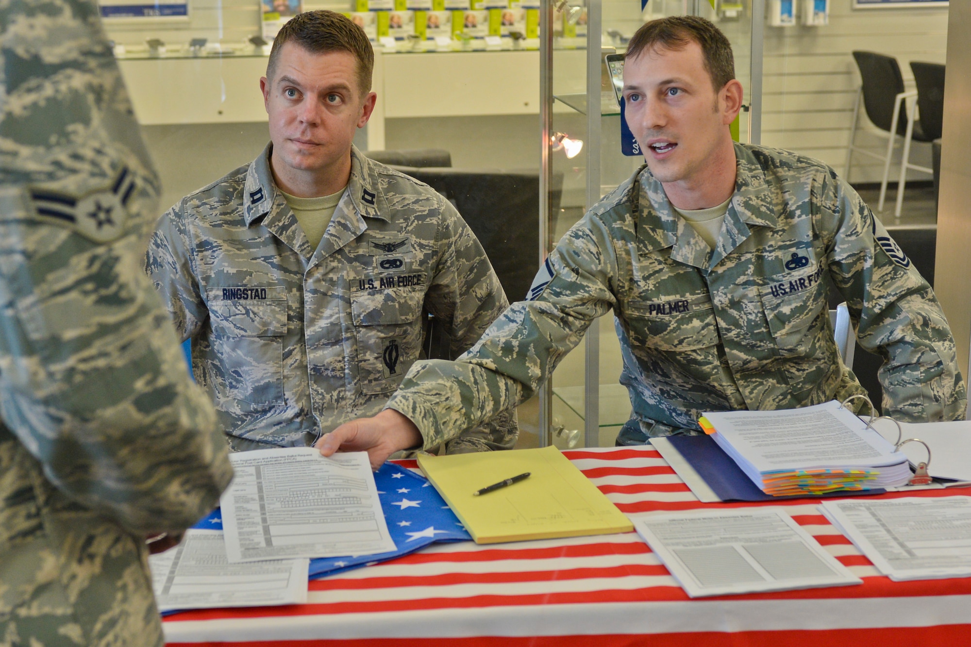 U.S. Air Force Capt. Erik Ringstad, 52nd Component Maintenance Squadron commander and Niceville, Fla., native, seated left, and U.S. Air Force Master Sgt. Timothy Palmer, 52nd CMS assistant accessory flight chief and Hobart, Ind., native, seated right, provide voter registration materials to U.S. Air Force Airman 1st Class Tyler Neff, a 52nd Security Forces Squadron patrolman and Bryson, Texas, native, at an information booth at the base exchange at Spangdahlem Air Base, Germany, June 30, 2014. The Federal Voting Assistance Program helps service members and their families with registration and voting guidelines across the United States.  (U.S. Air Force photo by Staff Sgt. Joe W. McFadden/Released)