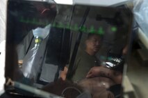 A reflection in an electrocardiogram shows Lt. Cmdr. Jeff Kang, director of training, Forward Resuscitative Surgical System team, 2nd Medical Battalion, 2nd Marine Logistics Group, observing as physicians care for a simulated casualty during pre-deployment training at Camp Lejeune, N.C., June 28, 2014.  Kang monitored the FRSS team’s progress during the training as they prepared for a future deployment.