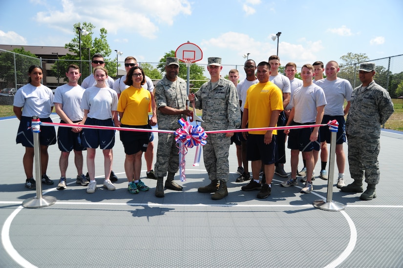 Col. Bill Knight, 11th Wing/Joint Base Andrews commander, and Chief Master Sgt. William Sanders, 11th WG/JBA command chief, pose for a ribbon cutting with dorm residents for official opening of the new volleyball and basketball court at Joint Base Andrews, Md., June 26, 2014. (U.S. Air Force photo/Airman 1st Class Joshua R. M. Dewberry)