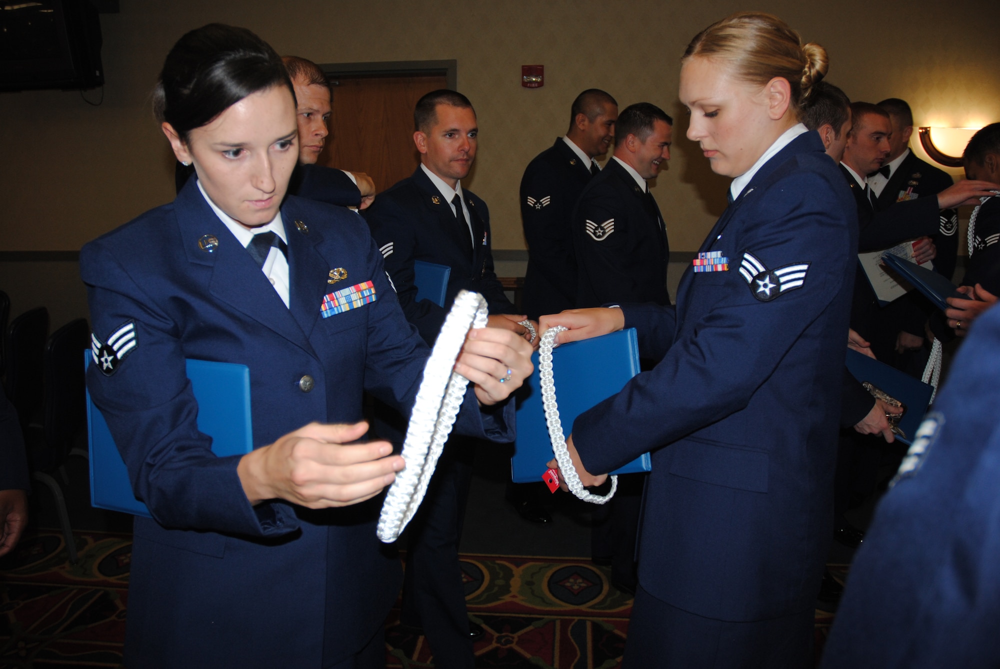 Members of ALS Class 14-Echo, remove the white aiguillettes after graduating from the Chief Master Sgt. Richard L. Etchberger Airman Leadership School during a graduation ceremony held June 26, 2014, at the Northern Lights Club on Grand Forks Air Force Base, N.D. ALS students wore the aiguillettes or white ropes on the left shoulder in order for people to recognize them as one of the graduates. Class 14-E was made up by two student flights. One flight consisted of 12 active-duty Airmen completing their in-residence course at the Etchberger ALS in Grand Forks AFB, while the other flight was made up of a dozen Air National Guard Airmen from the 119th Wing attending an in-residence ALS course at the North Dakota ANG base in Fargo, N.D. Both of the flights were simultaneously taught by Air Force active-duty instructors from the Etchberger ALS. This new approach on training was the first of its kind according to officials from the 119th Wing and the 319th Air Base Wing. (U.S. Air Force photo/Staff Sgt. Luis Loza Gutierrez)