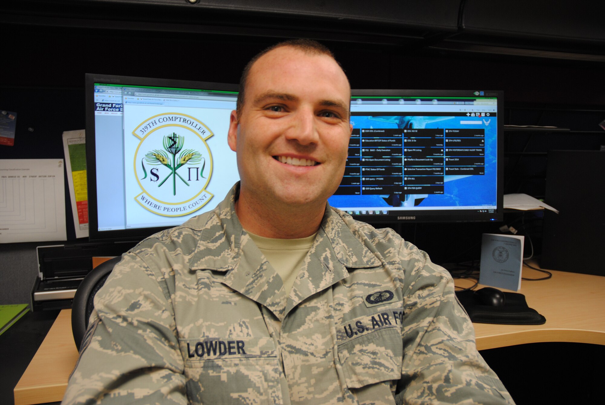 With his squadron shield proudly displayed behind him, Senior Airman Jeffrey M. Lowder, 319th Comptroller Squadron financial analysis supervisor, poses for a photo  on July 2, 2014, at his work station on Grand Forks Air Force Base, N.D. The 28-year-old from Camden, S.C., was named base's Warrior of the Week for the first week of July 2014. (U.S. Air Force photo/Staff Sgt. Luis Loza Gutierrez)
