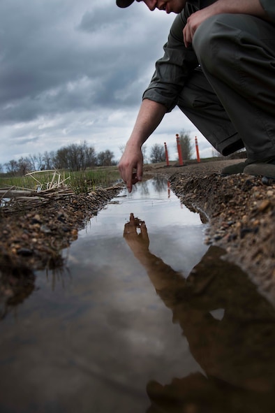 Senior Airman Nathaniel Boober, 5th Civil Engineer Squadron insect control, searches a puddle of standing water in hopes of identifying a mosquito breeding ground on Minot Air Force Base, May 19, 2014. Once Boober identifies where most of the larvae are, he can more effectively reduce the amount of mosquitoes on base. (U.S. Air Force photos/Airman 1st Class Lauren Pitts) 