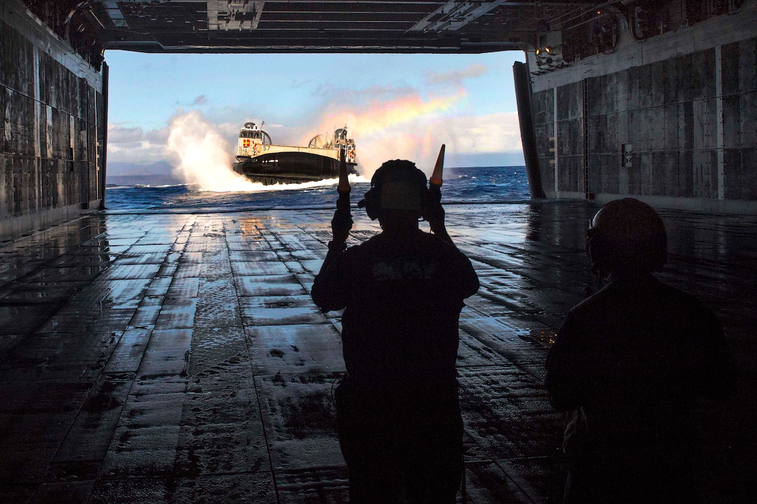 U.S. Navy Petty Officer 2nd Class Brooks Graham, left, directs a landing craft air cushion into the well deck of the USS Peleliu following a training exercise in the Pacific Ocean, June 25, 2014. Graham is a boatswain's mate. The Peleliu is en route to Hawaii to participate in Rim of the Pacific 2014. Twenty-two nations, more than 40 ships and submarines, more than 200 aircraft and 25,000 personnel are participating in the exercise 