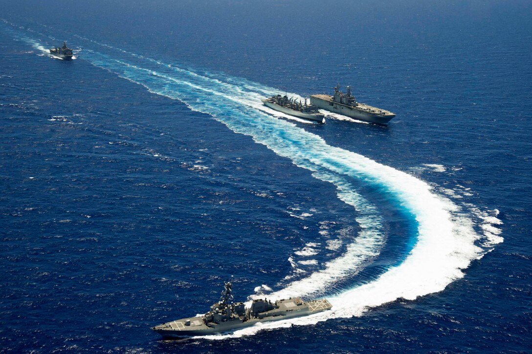 The guided-missile destroyer USS Spruance, foreground, pulls away as the amphibious dock landing ship USS Rushmore approaches the Military Sealift Command fast combat support ship USNS Rainier, center, in the Pacific Ocean, June 24, 2014. The amphibious assault ship USS Peleliu is conducting a replenishment-at-sea with the Rainier. The ships are en route to participate in the Rim of the Pacific 2014 exercise. 