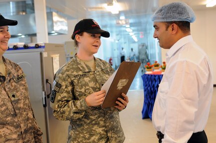 Army Spc. Crystal Stoner speaks with a contractor at the dining facility, as her mother, Spc. Theresa Stoner, looks on Jan. 30. The Stoners are assigned to the 230th Engineer Battalion as food service specialists at the dining facility. Crystal uses the knowledge she gained from advanced individual training to better serve Third Army service members here at the dining facility. Their support in food service helps ensure everyone receives the support they need to continue their missions.