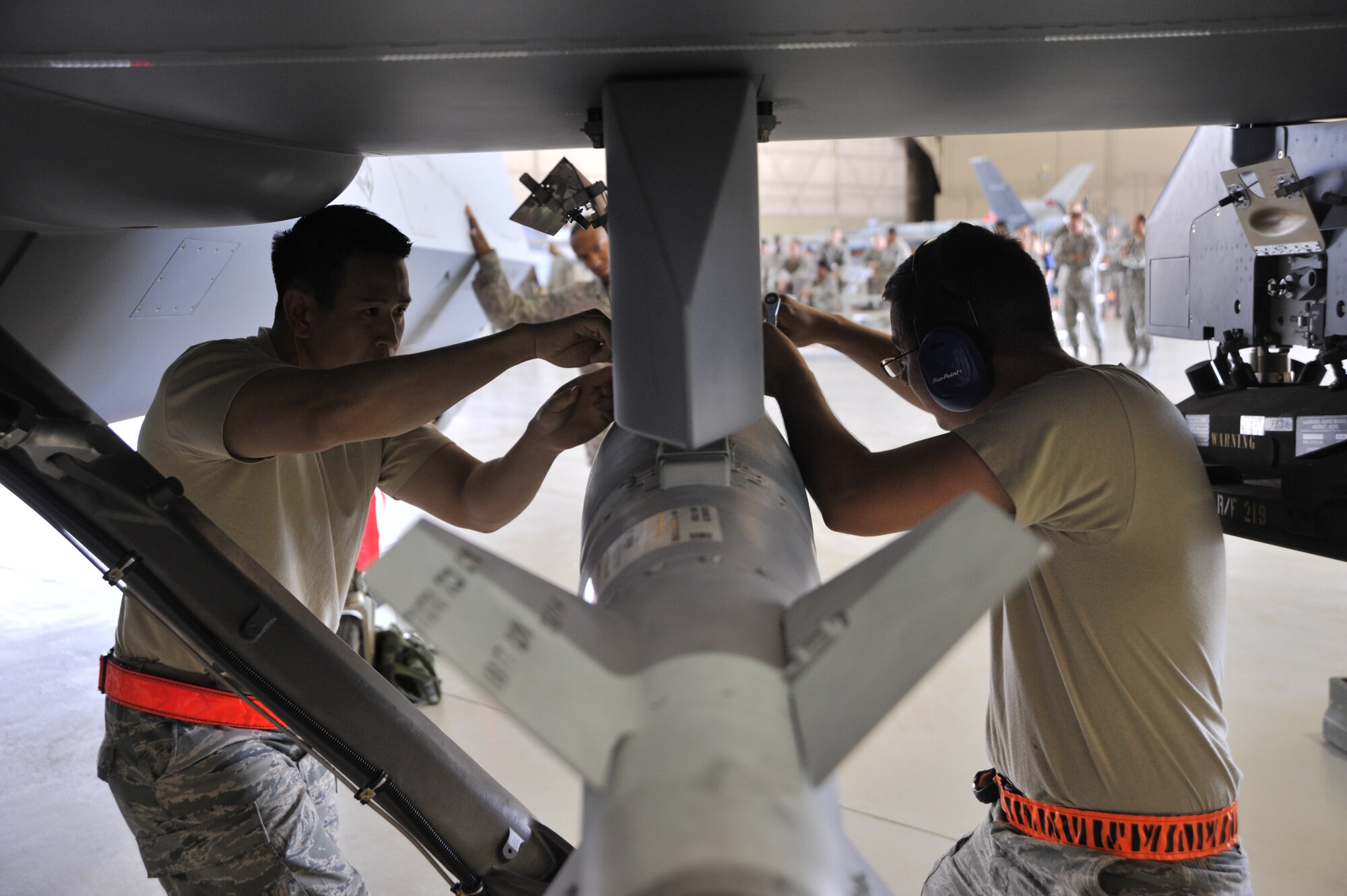 Staff Sgt. Trung Dinh, 432nd Aircraft Maintenance Squadron weapons load crew chief, left, and Senior Airman Devin Milburn, 432nd Aircraft Maintenance Squadron support technician, attach a GBU-12 Paveway laser guided bomb onto an MQ-9 Reaper during a load crew competition at Creech Air Force Base, Nev., June 30, 2014. The competition consists of two three-man teams from different aircraft maintenance units competing against each other in order to build skills and promote camaraderie. (U.S. Air Force photo by Airman 1st Class Christian Clausen/Released)