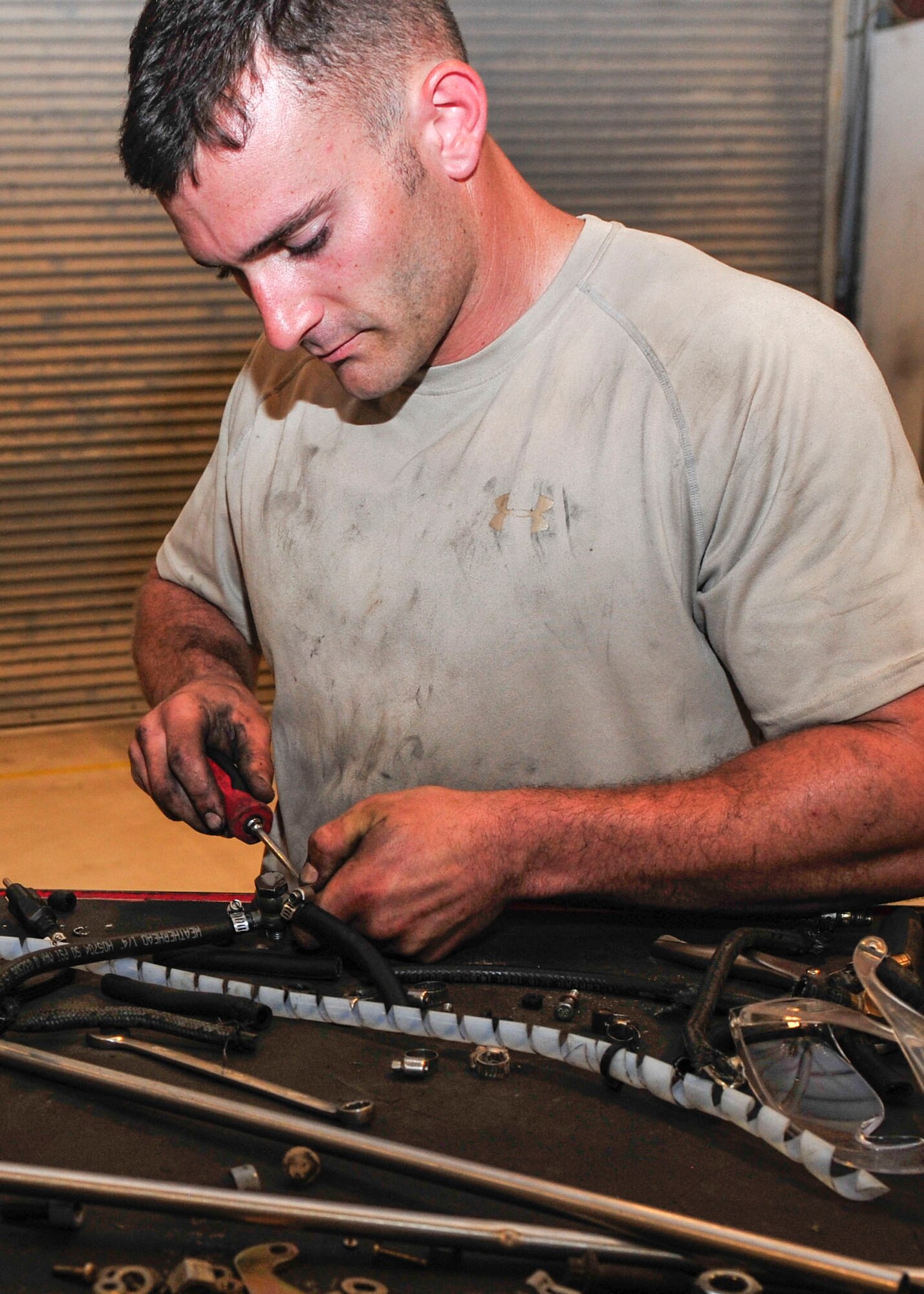 U.S Air Force Senior Airman Tyler Thibault, 379th Expeditionary Maintenance Squadron Aerospace Ground Equipment maintenance journeyman tightens a clamp on a hose at Al Udeid Air Base, Qatar, June 30, 2014. The AGE flight provides maintenance stands, electricity, equipment used to load munitions to support aircraft assigned at Al Udeid. Thibault is deployed from Ellsworth Air Force Base, South Dakota and his hometown is New Orleans. (U.S. Air Force photo by Senior Airman Colin Cates)
