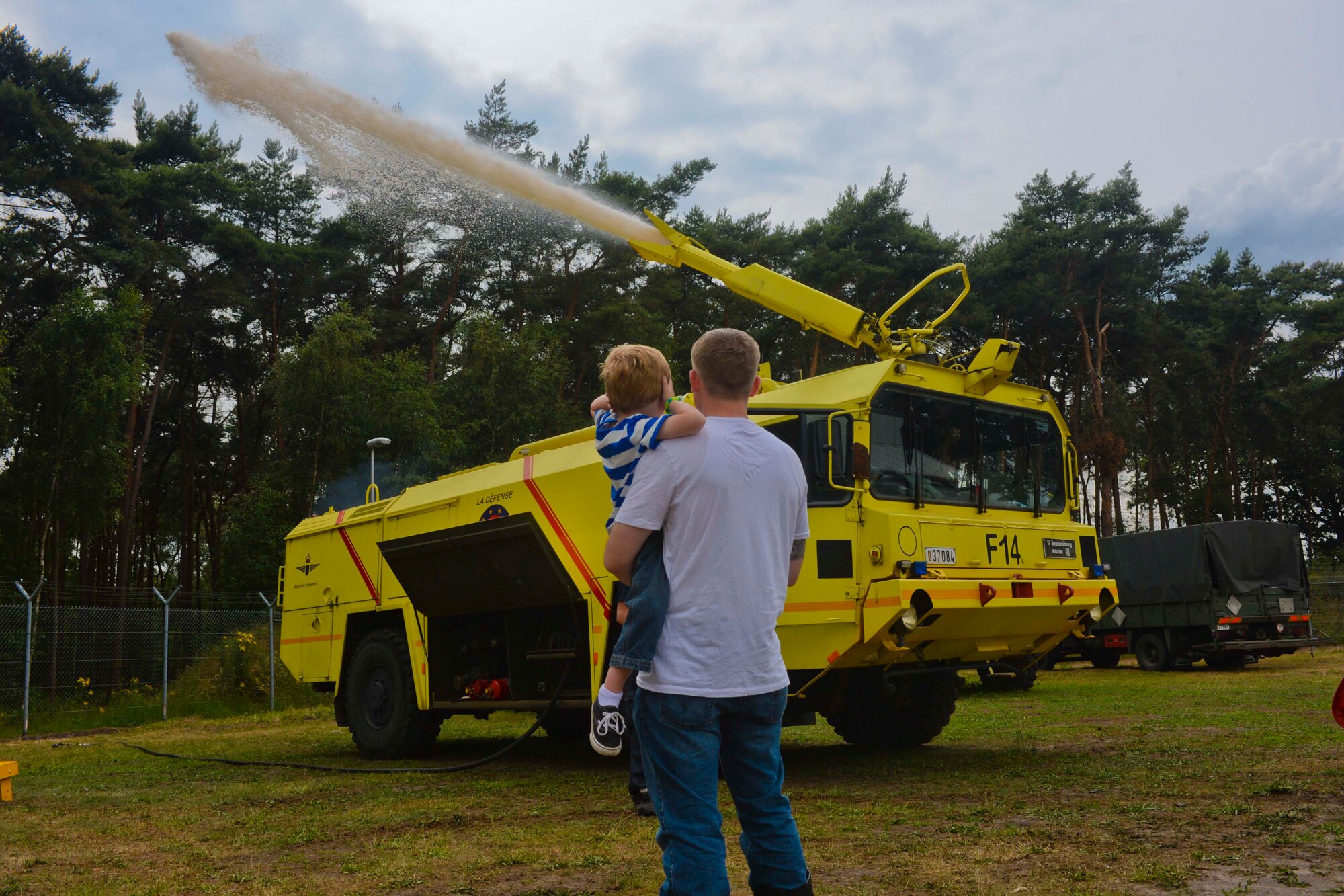 U.S. Air Force Staff Sgt. Evan McLelland, a 701st Munitions Support Squadron NCO and Boynton Beach, Fla., native, holds his son, Aiden, 5, as they watch a Belgian Air Component fire truck shoot its water cannon during the Belgian-American Friendship Day at Kleine Brogel Air Base, Belgium, June 27, 2014.  The Belgian Armed Forces maintain the installation which houses the Airmen of the 701st MUNSS. (U.S. Air Force photo by Staff Sgt. Joe W. McFadden/Released)