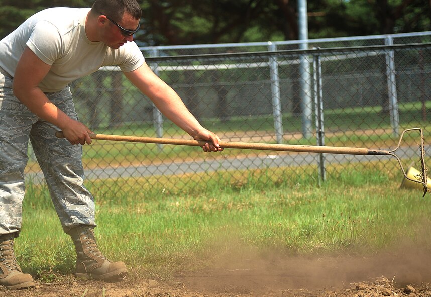 U.S. Air Force Airman 1st Class William Klein, 35th Civil Engineer Squadron heavy equipment and pavements journeyman, rakes shrubs around the perimeter of the Leftwich Park baseball field at Misawa Air Base, Japan, July 2, 2014. Klein was part of a team of 35 CES Airmen who helped make the final touches to the revamping of the baseball field. (U.S. Air Force photo/Senior Airman Jose L. Hernandez-Domitilo)