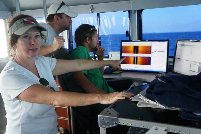 Archaeologist Wendy Weaver (left) and Florida II crew members Matt Staley (center) and Chad Harralson (right) review data in real time as they tow the equipment in transects over a pre-selected area. The left monitor shows the sub-bottom profiler with results in orange and the side scan sonar on the right. The magnetometer readings are visible on the far right monitor.