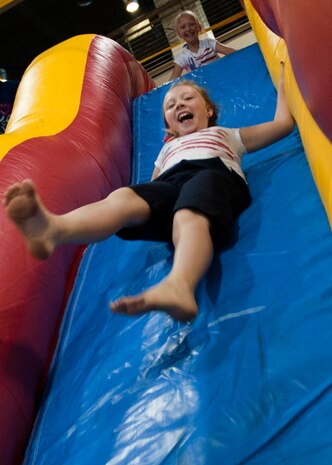 Jenna-Lynn slides down an inflatable slide, while her sister Cara-Leigh watches and waits, during Freedom Fest July 3, 2014 at Nellis Air Force Base Nev. Freedom Fest, hosted by the 99th Force Support Squadron, provided Airmen and their families a chance to wind down before the four day weekend. (U.S. Air Force photo by Senior Airman Timothy Young)