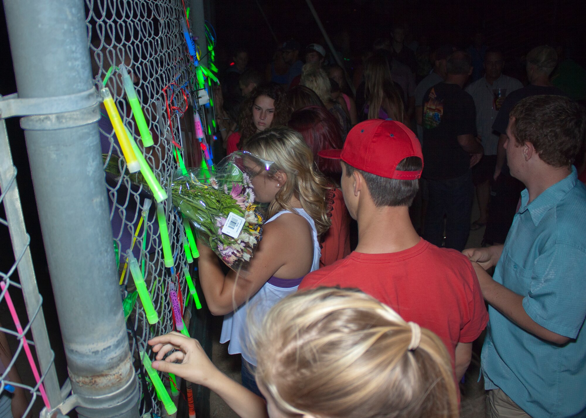 Desert Junior Senior High School students, family and friends, hang their glow sticks on the DHS baseball field backstop and sign memorial portraits for John Burgess and Christopher Ricker July 2. (Courtesy photo by Master Sgt. John McGee)