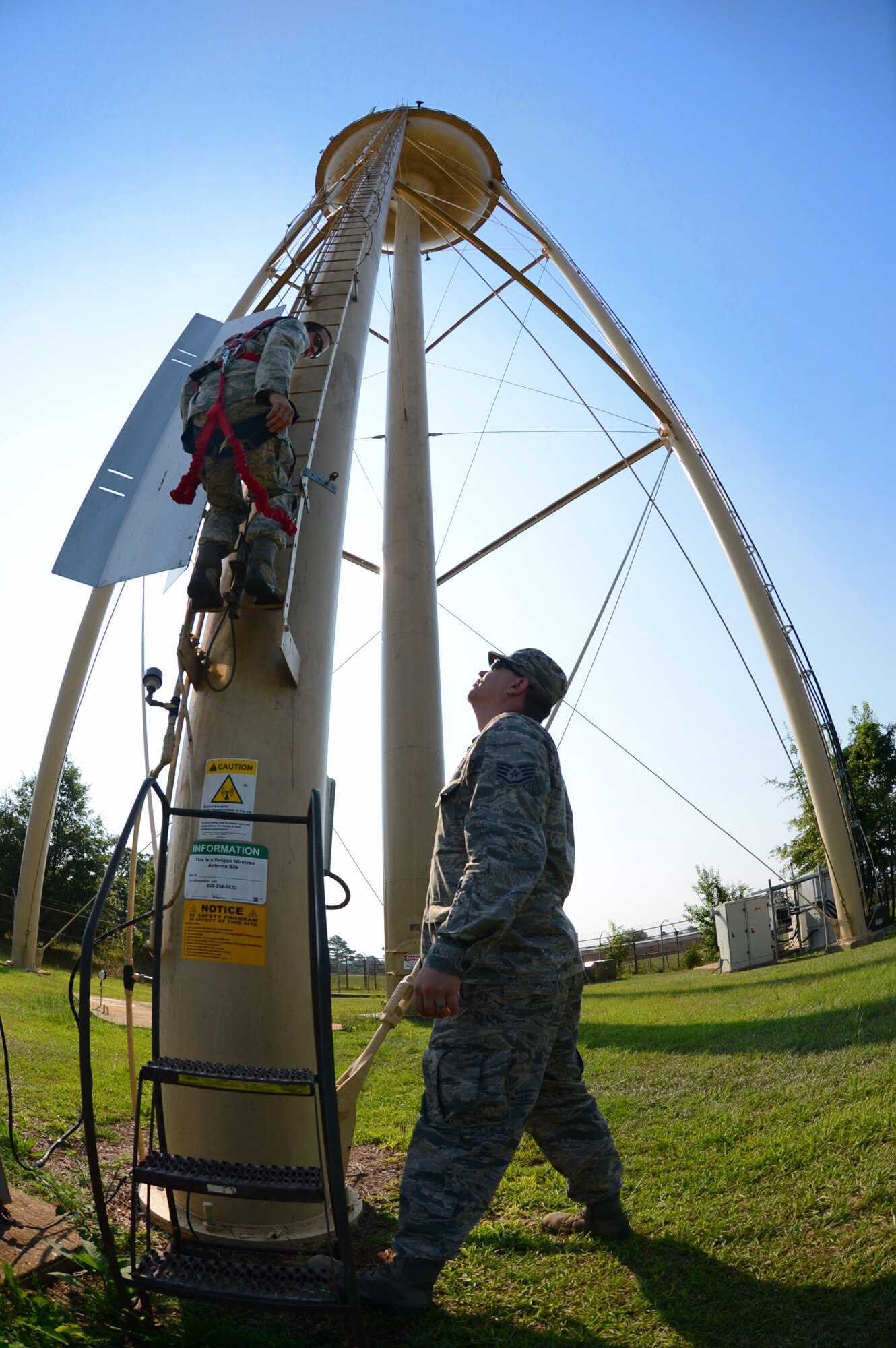 U.S. Air Force Staff Sgt. Phillip Coley, 20th Civil Engineer Squadron water and fuels systems maintenance craftsman, hooks onto a water tower ladder while Staff Sgt. Brian Joki, 20th CES water operations supervisor, “spots” the ladder at Shaw Air Force Base, S.C., July 8, 2014. Coley climbed the 120 foot tower during a yearly maintenance inspection. (U.S. Air Force photo by Airman 1st Class Jensen Stidham/Released)