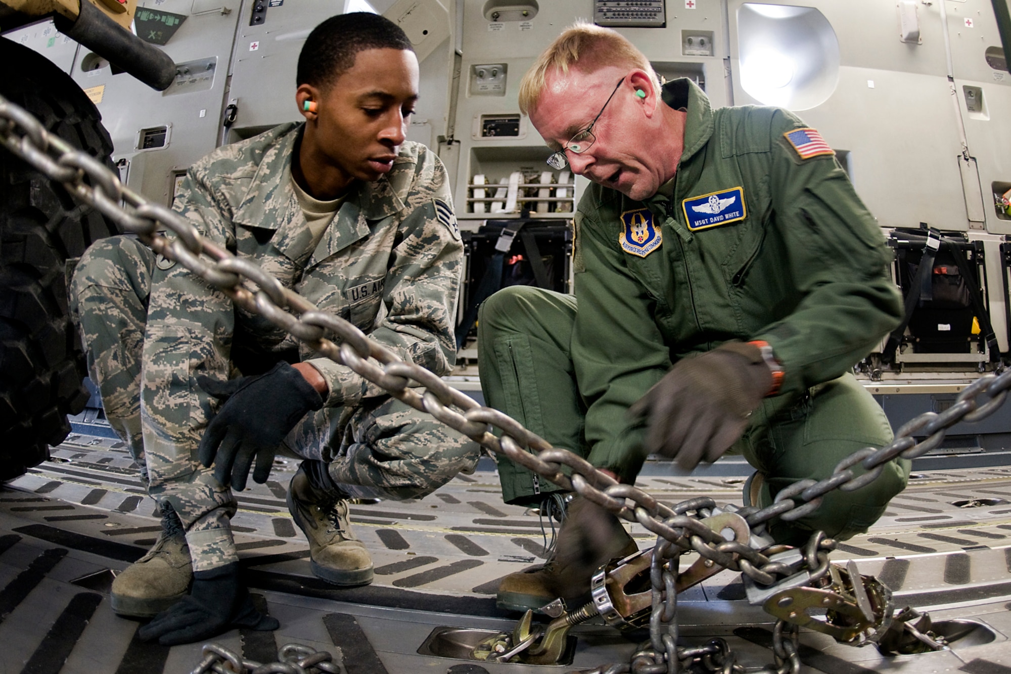 U.S. Air Force Master Sgt. David White, 89th Airlift Squadron loadmaster, shows U.S. Air Force Senior Airman Rickey Davis, 49th Aerial Port Squadron aerial port specialist, how he ties down heavy trucks inside a C-17 Globemaster III aircraft at Grissom Air Reserve Base, Ind., May 3, 2014. Airmen of Grissom's 49th APF and Airmen from the 89th AS, based at Wright-Patterson Air Force Base, Ohio, took a day to show U.S. Army Reserve 766th Transportation Battalion Soldiers how to build cargo pallets for airlift and how to load a Humvee and a HEMTT into a C-17 Globemaster III aircraft. (U.S. Air Force photo/Tech. Sgt. Mark R. W. Orders-Woempner)

