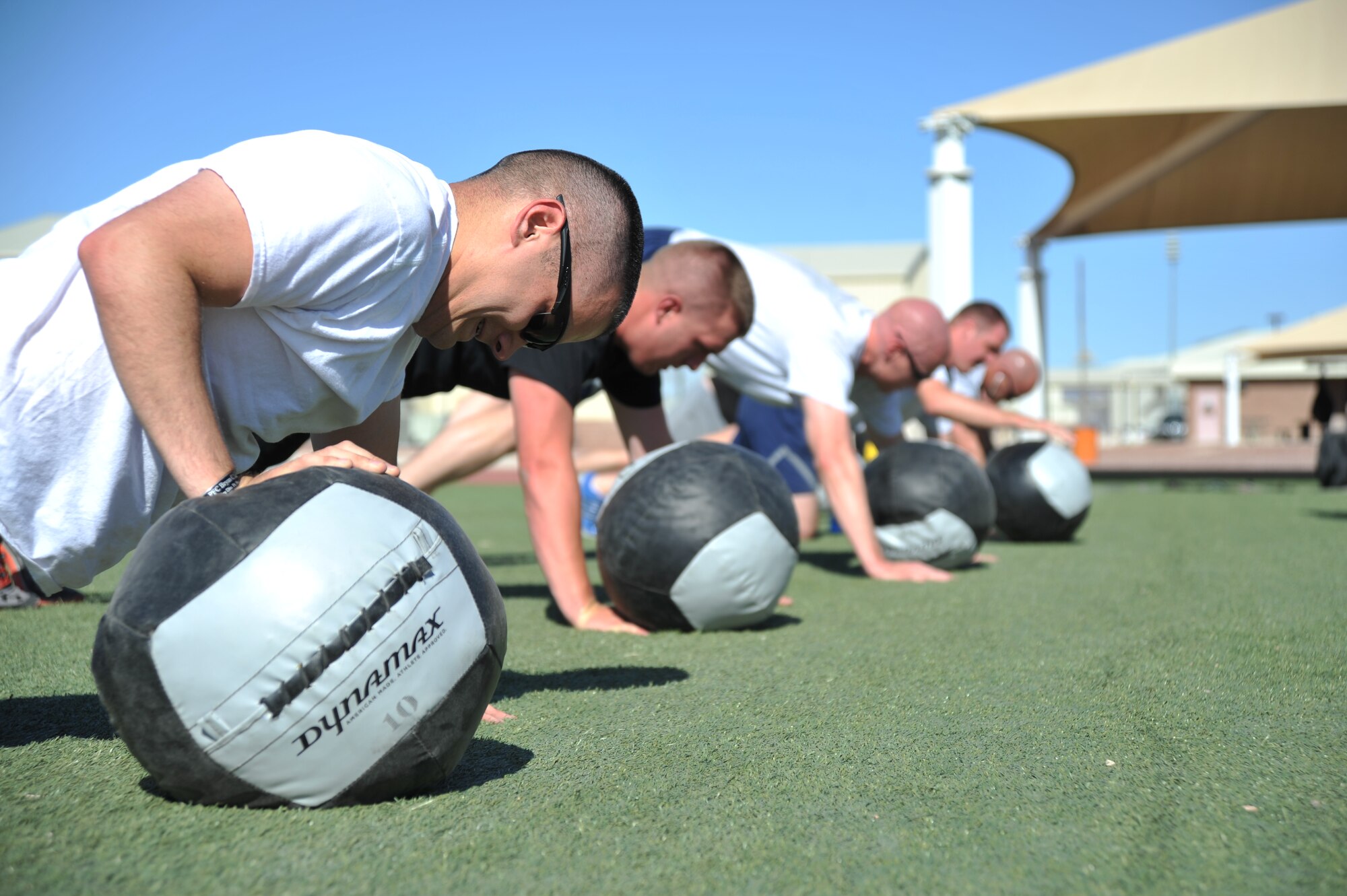 1st Lt. Matt Cole, 99th Ground Combat Training Squadron logistics officer in charge, and Creech Airmen perform a one-arm pushup with a medicine ball during a Warrior Trained Fitness event June 23, 2014, at Creech Air Force Base, Nev. The Life of a Warrior campaign focuses on the whole-person concept to include the physical, mental, social and spiritual pillars of resiliency. (U.S. Air Force photo by Tech. Sgt. Shad Eidson/Released)