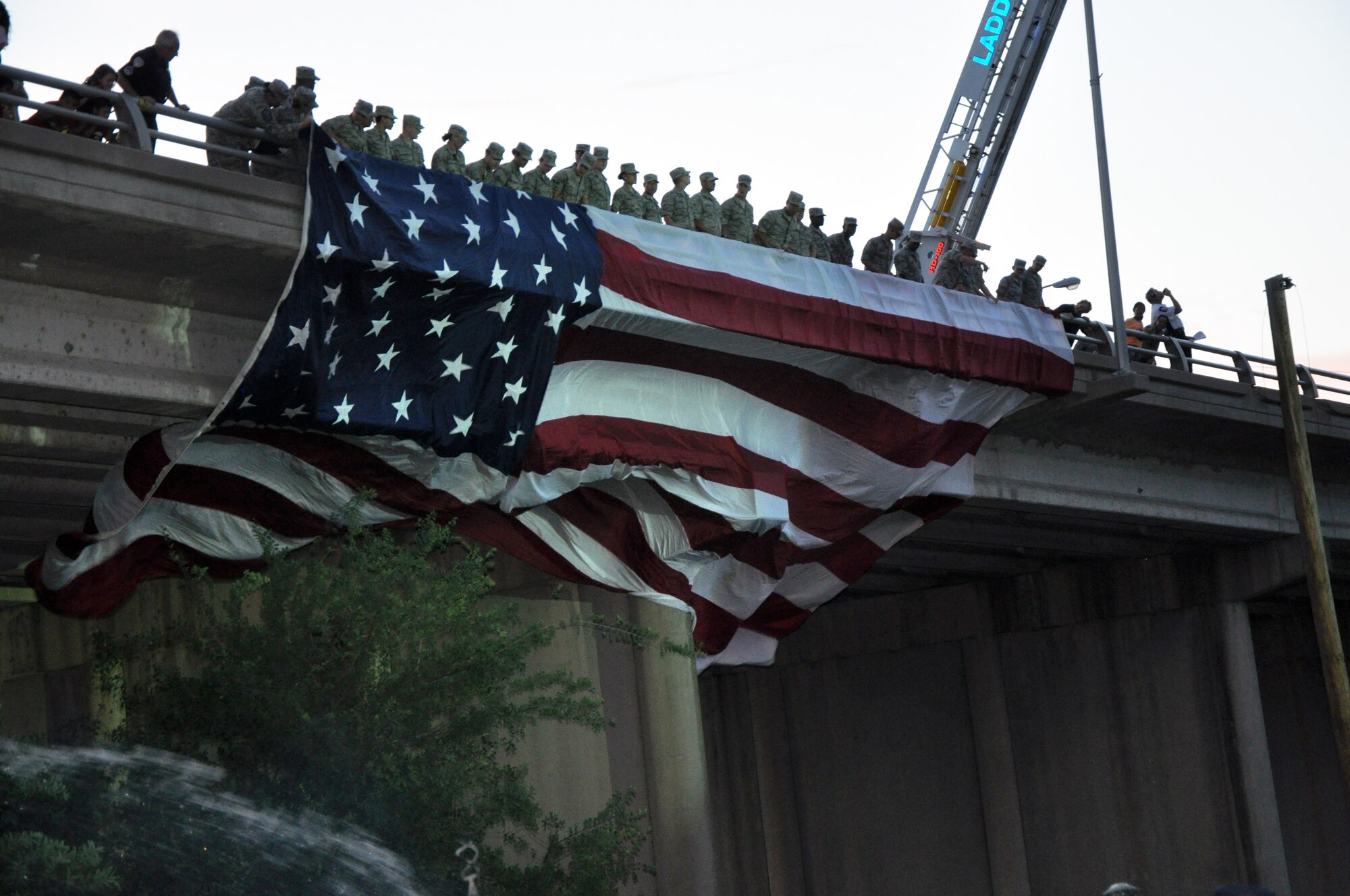 SAN ANGELO, Texas – Goodfellow Airmen drape a U.S. flag from the South Chadbourne Street Bridge during the Annual Pops Concert at the Bill Aylor Sr. Memorial RiverStage here July 3. Volunteers from all the branches of the military assisted at the concert with various services. (U.S. Air Force photo/ Senior Airman Joshua Edwards)