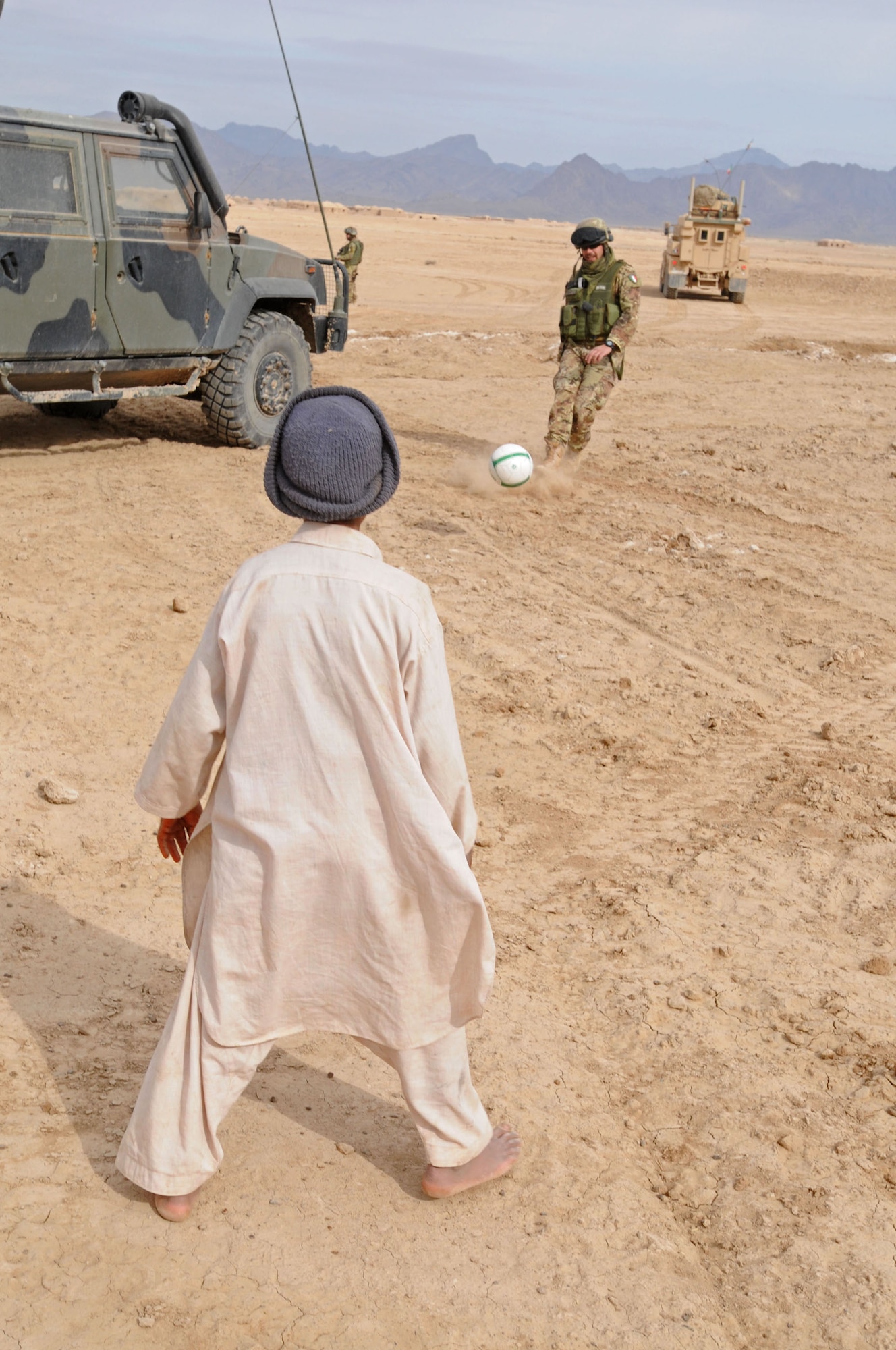 An Italian soldier plays soccer with a young Afghan boy during a visit to a local village in Bakwa district, Farah Province in 2011. With the help of coalition forces and U.S. Agency for International Development, many new soccer pitches have been erected in western Afghanistan. (U.S. Navy Photo by Mass Communications Specialist 1st Class Stephen Hickok/RELEASED)
