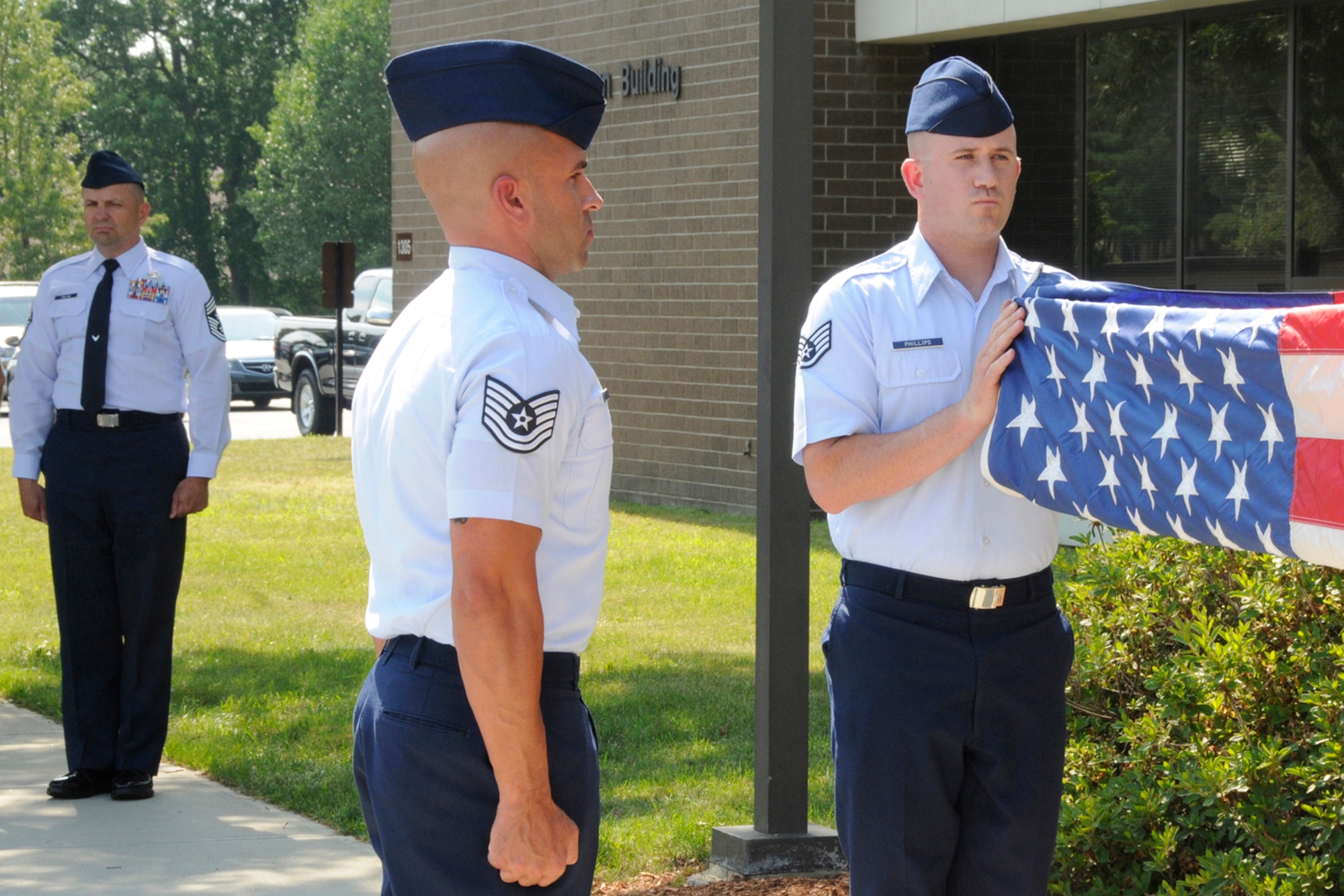 HANSCOM AIR FORCE BASE, Mass. -- Staff Sgt. Kevin Phillips (right) and Tech. Sgt. Jason Jernigan (left), Patriot Honor Guard members, retrieve the flag during a retreat ceremony outside Building 1305 July 7, while Command Chief Master Sgt. Craig A. Poling stands nearby. Members of 66th Air Base Group participated along with Patriot Honor Guard in the formal retreat ceremony. (U.S. Air Force photo by Linda LaBonte Britt)