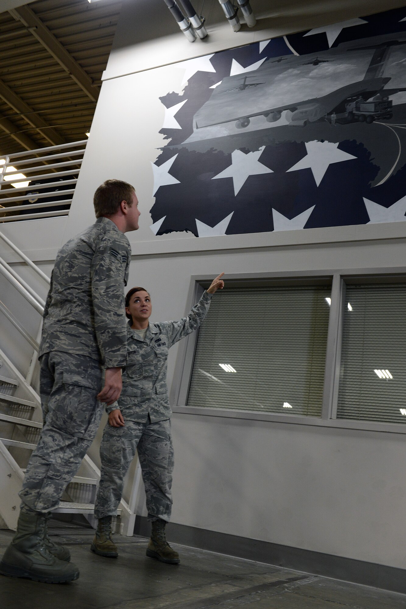 Senior Airman Brittany Kieffer, 62nd Aerial Port Squadron cargo processing element member, shows Senior Airman Phillip Smith, 62nd APS cargo processing shift supervisor, a section of a mural she painted July 11, 2014, at Joint Base Lewis-McChord, Wash. Painting the mural in her off time utilizing her own resources, Kieffer completed the mural in two months. This is the second mural she has painted for the Airmen of Team McChord. (U.S. Air Force photo/Airman 1st Class Jacob Jimenez)