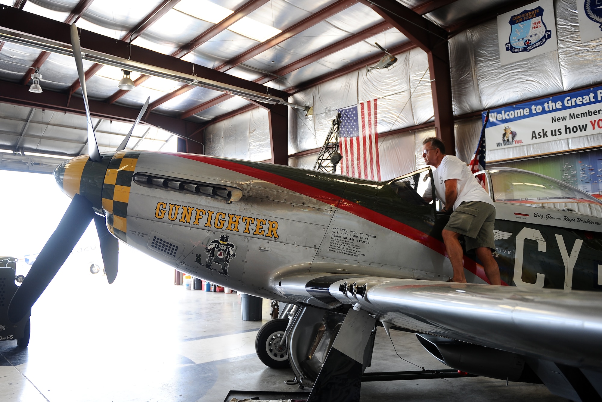 Larry Lumpkin, P-51 Gunfighter Mustang pilot, stands on the wing of the aircraft as he prepares to pull it from a hangar located at the Council Bluffs Municipal Airport, Iowa, on June 27. Lumpkin has amassed more than 700 hours in the in the Mustang cockpit performing an average of eight-to-ten air shows annually.  (U.S. Air Force photo by Josh Plueger/Released)