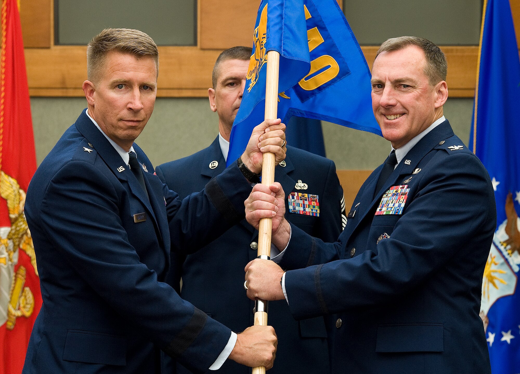 Brig. Gen. Patrick J. Doherty, Director of Air Force Services, Headquarters U.S. Air Force, Washington, D.C., presents the Air Force Mortuary Affairs Operations guidon to Col. Daniel F. Merry, the new AFMAO commander, during a change of command ceremony July 11, 2014 in the atrium of the Charles C. Carson Center for Mortuary Affairs, Dover Air Force Base, Del.  (U.S. Air Force photo/Roland Balik)