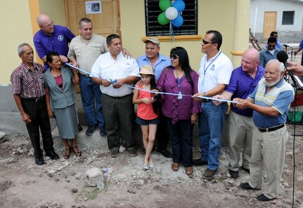 Joint Task Force-Bravo, Honduras Habitat for Humanity-Siguatepeque region, Municipality of Ajuterique officials and other volunteers cut the ribbon during a Habitat for Humanity house dedication in Ajuterique, Department of Comayagua, Honduras, July 5, 2014 where 18 local families received the keys to their new homes.  Volunteers from JTF-Bravo worked over 600 hours on Saturdays filling trenches, leveling ground and shoveling dirt at the Ajuterique Housing Project helping these Honduran families construct their homes.  (Photo by U. S. Air National Guard Capt. Steven Stubbs)